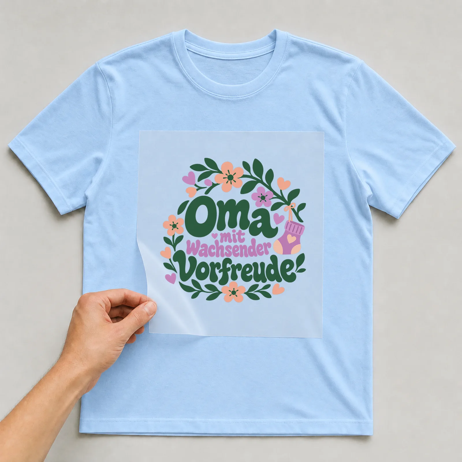 Bügelbild „Oma mit wachsender Vorfreude“ auf hellblauem T-Shirt, Folie wird aufgelegt