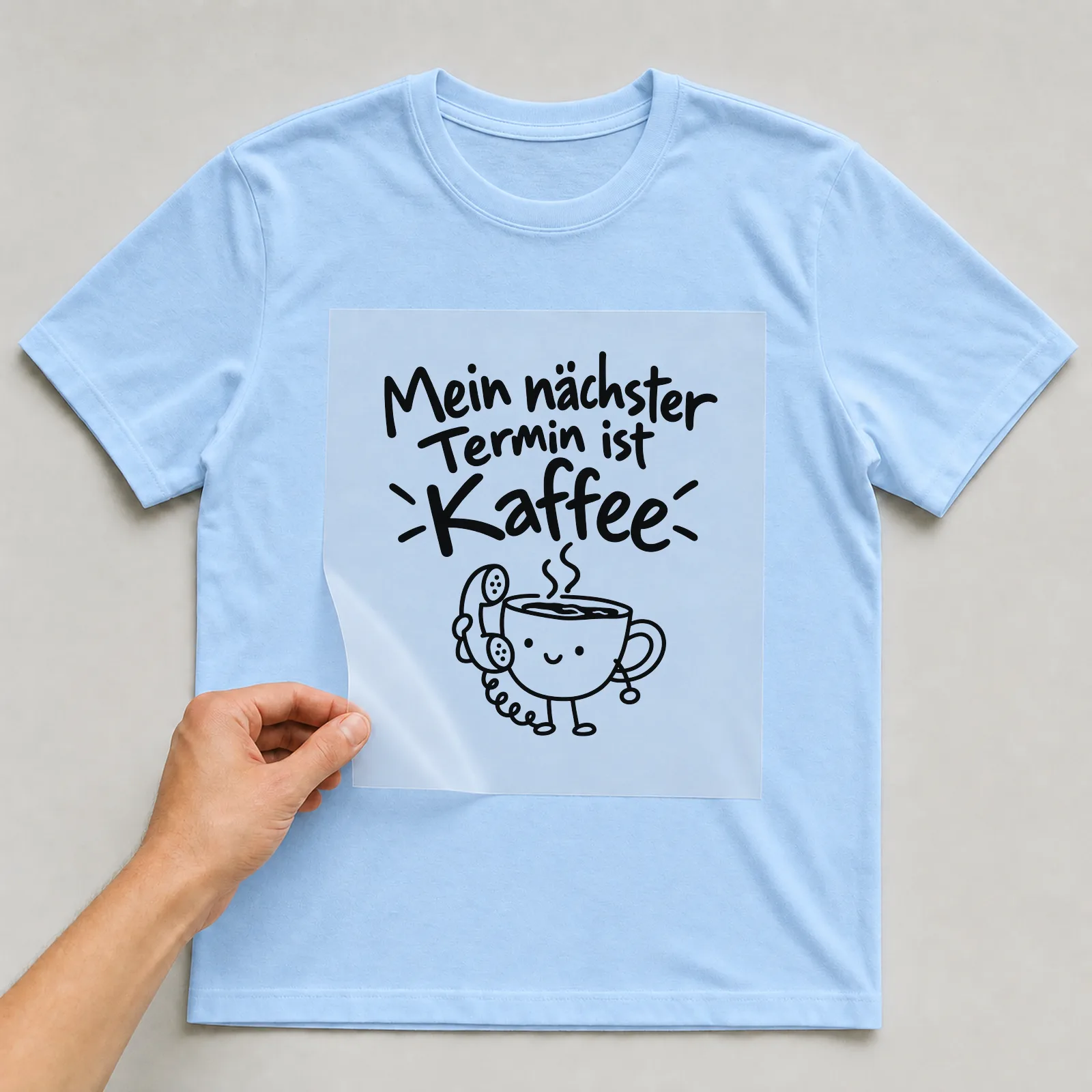 Bügelbild „Mein nächster Termin ist Kaffee“ auf hellblauem T-Shirt, Folie wird aufgelegt