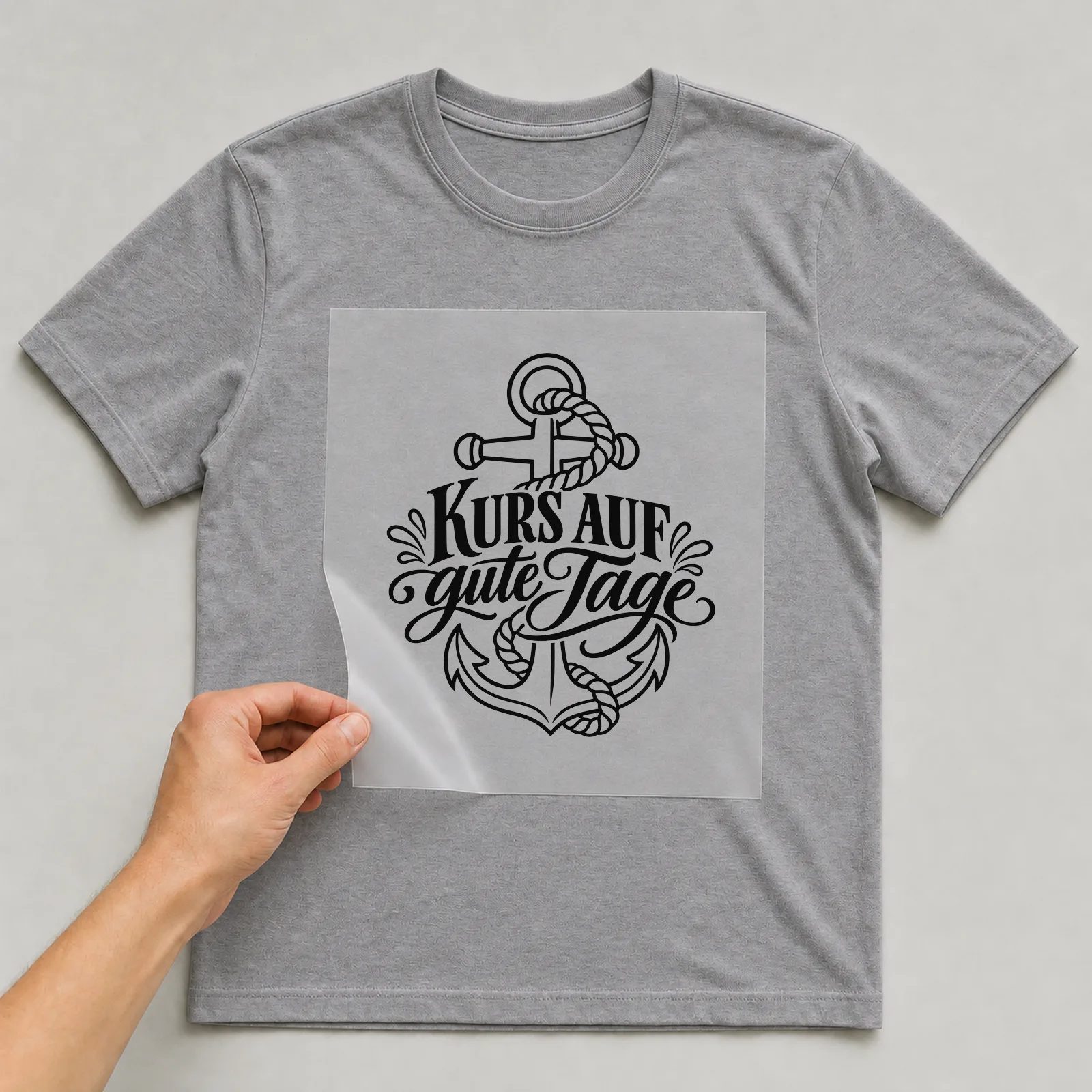Bügelbild „Kurs auf gute Tage“ auf grauem T-Shirt, Folie wird aufgelegt