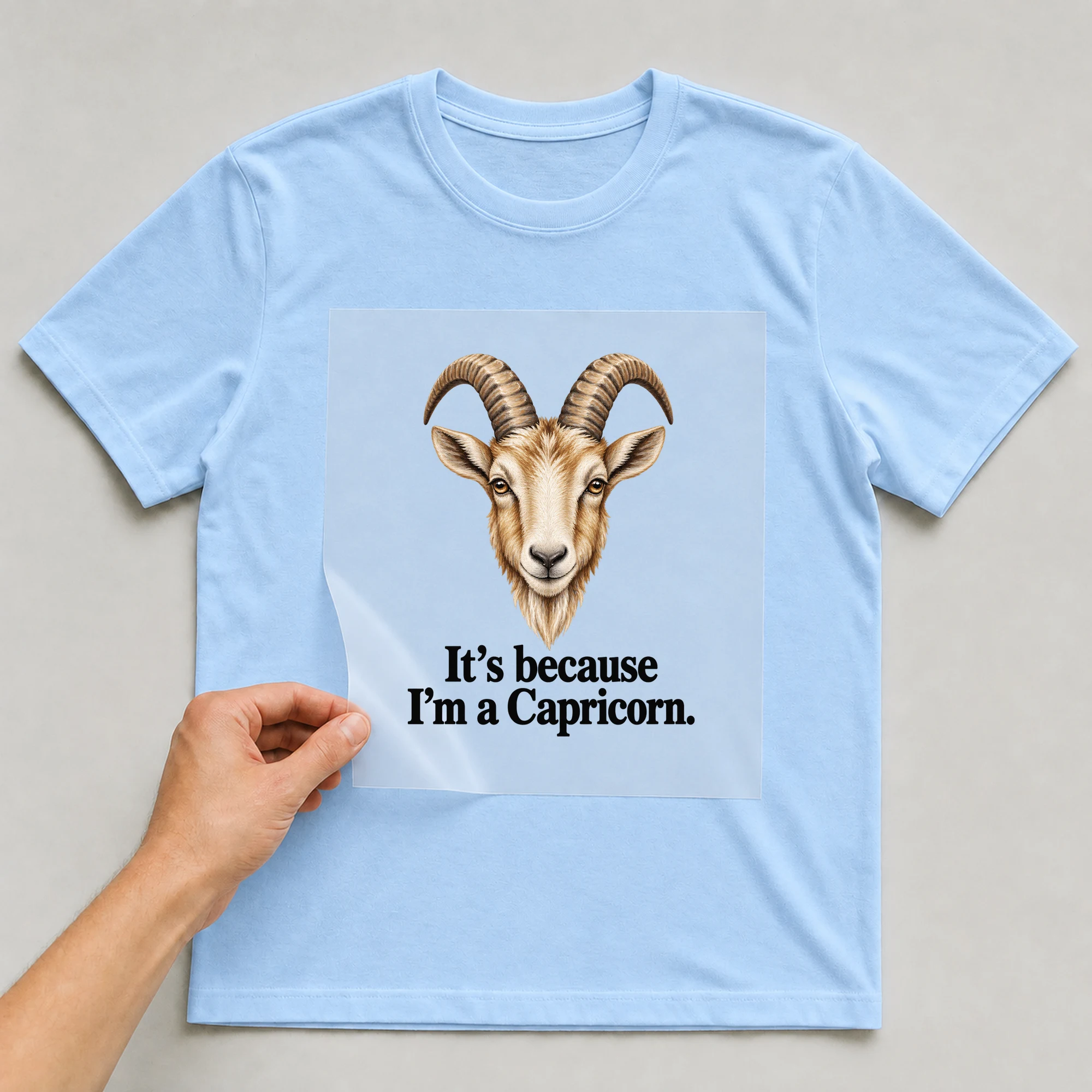 Bügelbild „It's because I'm a Capricorn.“ auf babyblauem T-Shirt, Folie wird aufgelegt