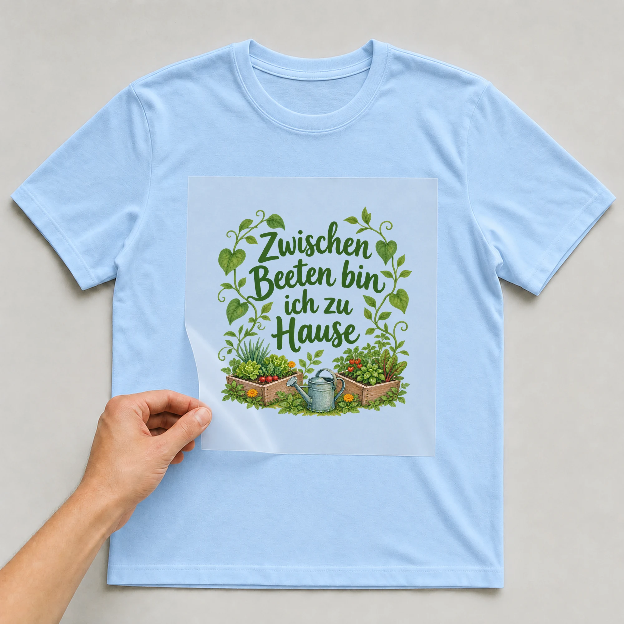 Bügelbild „Zwischen beeten bin ich zu hause“ auf babyblauem T-Shirt, Folie wird aufgelegt