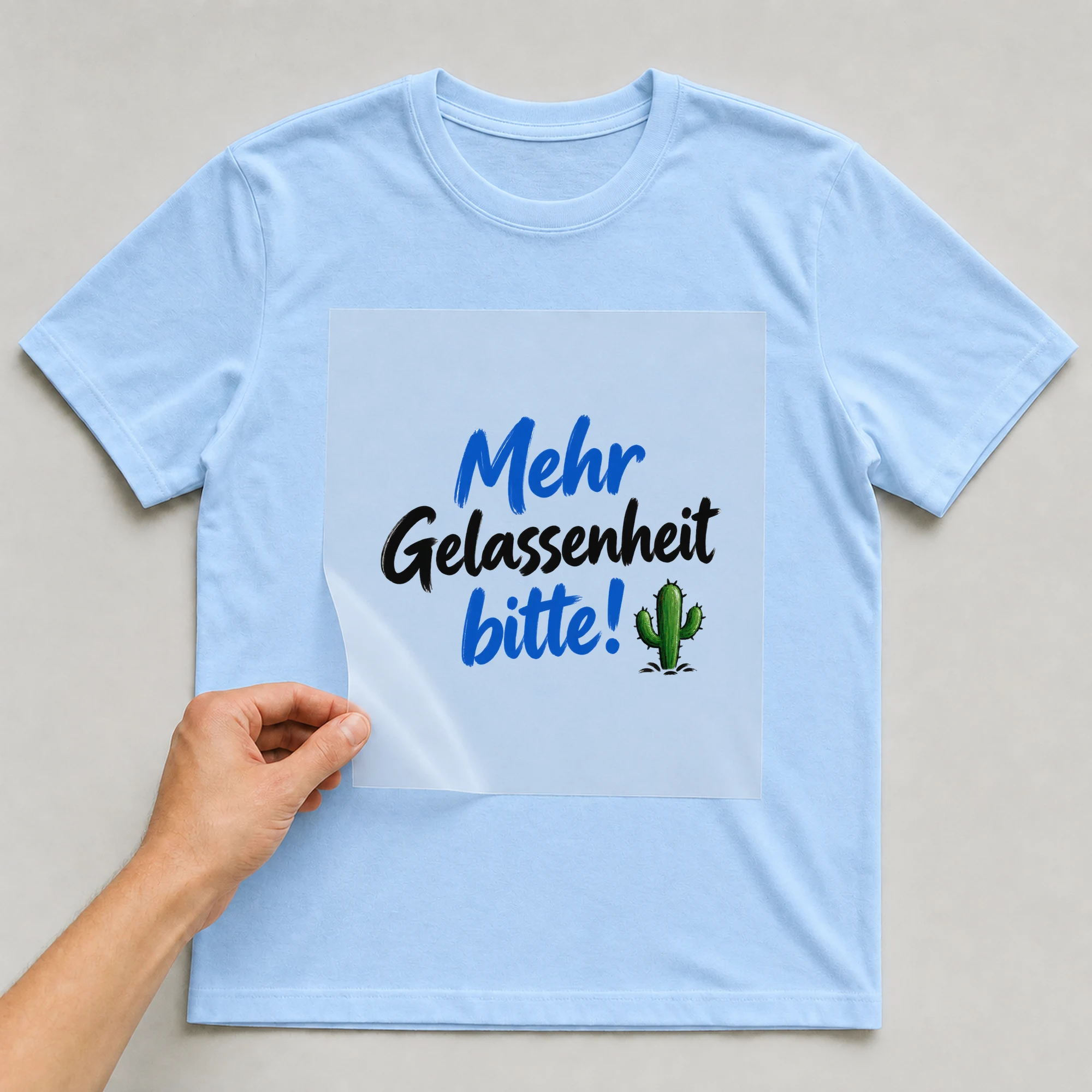 Bügelbild „Mehr Gelassenheit bitte!“ auf babyblauem T-Shirt, Folie wird aufgelegt