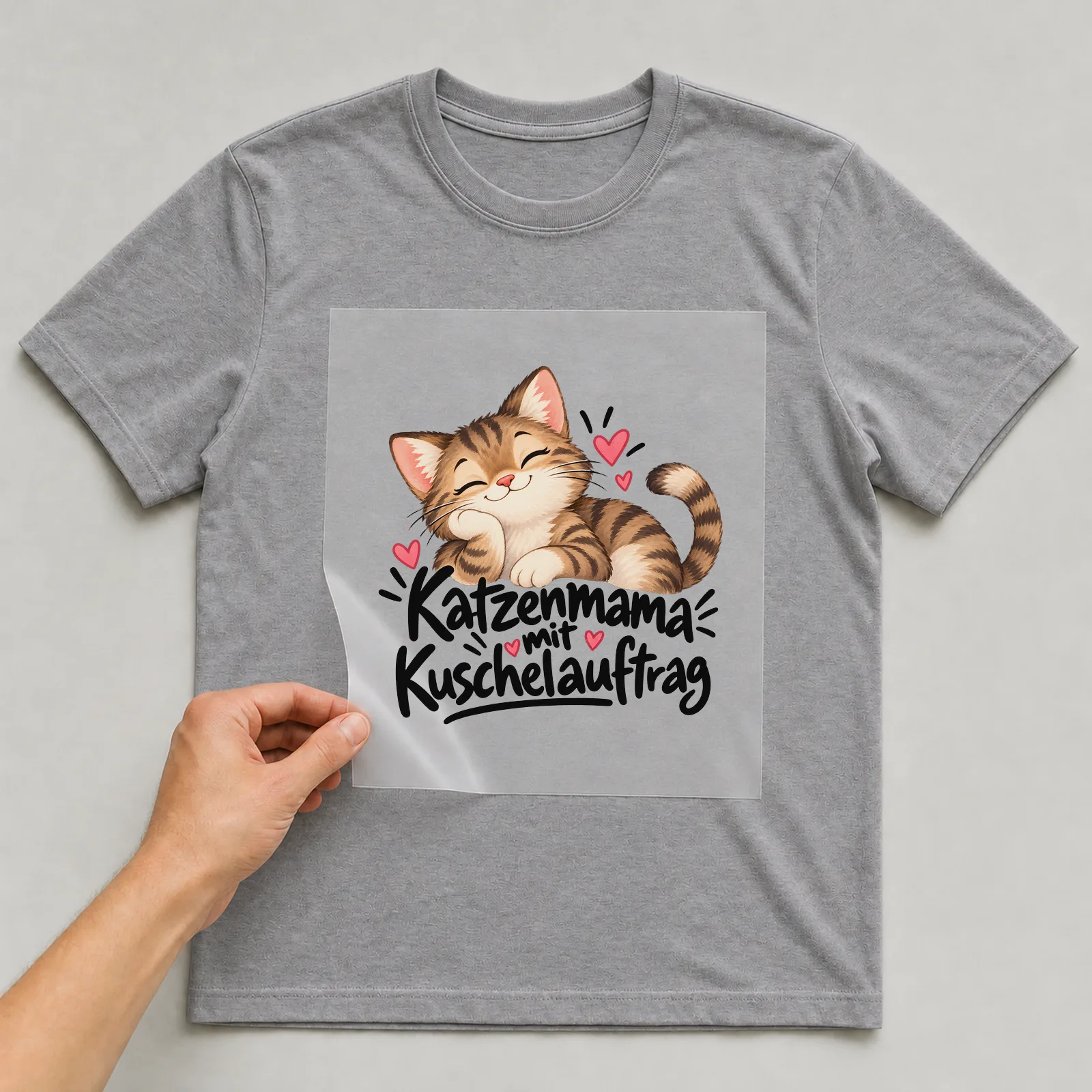 Bügelbild „Katzenmama mit Kuschelauftrag“ auf grauem T-Shirt, Folie wird aufgelegt