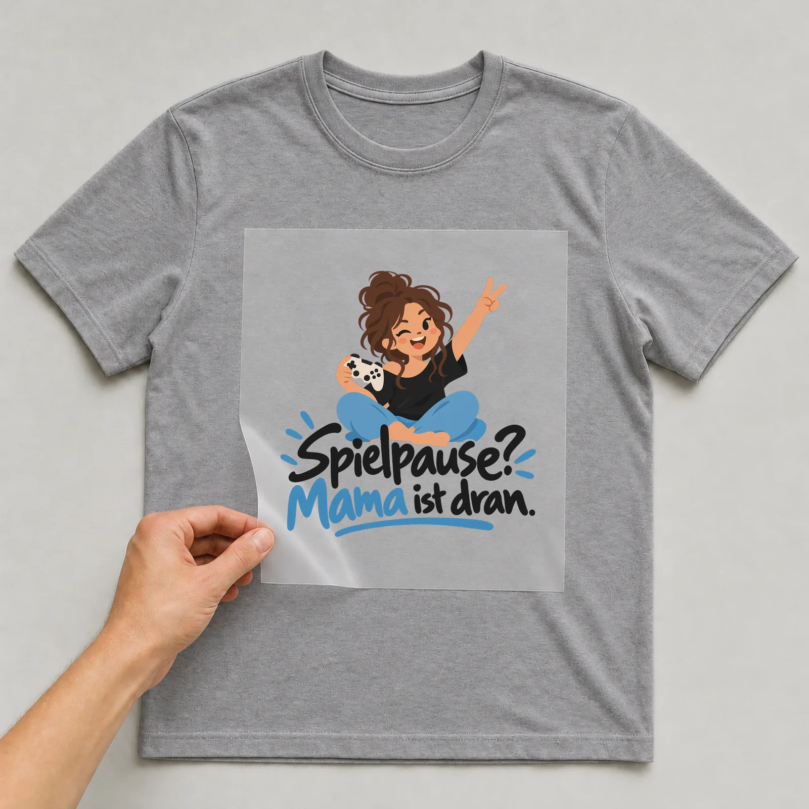 Bügelbild „Spielpause? Mama ist dran.“ auf grauem T-Shirt, Folie wird aufgelegt