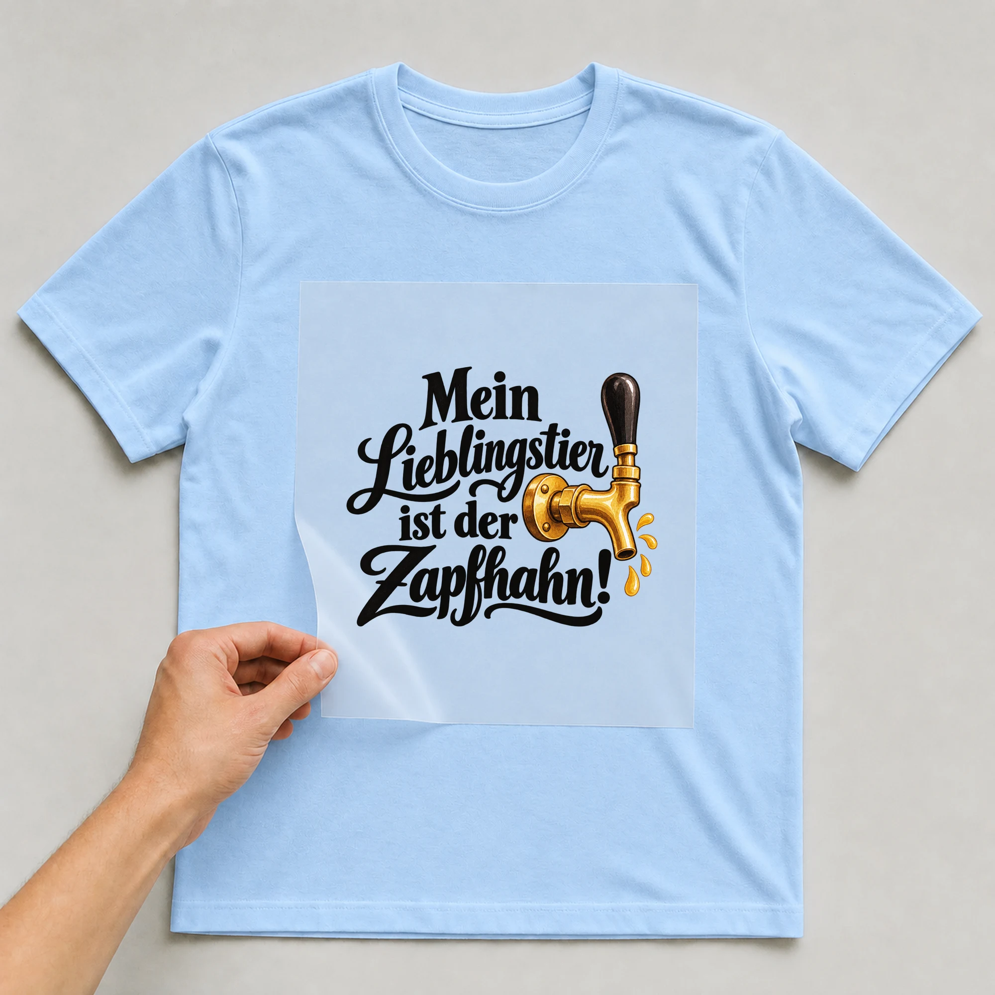 Bügelbild „Mein Lieblingstier ist der Zapfhahn!“ auf babyblauem T-Shirt, Folie wird aufgelegt