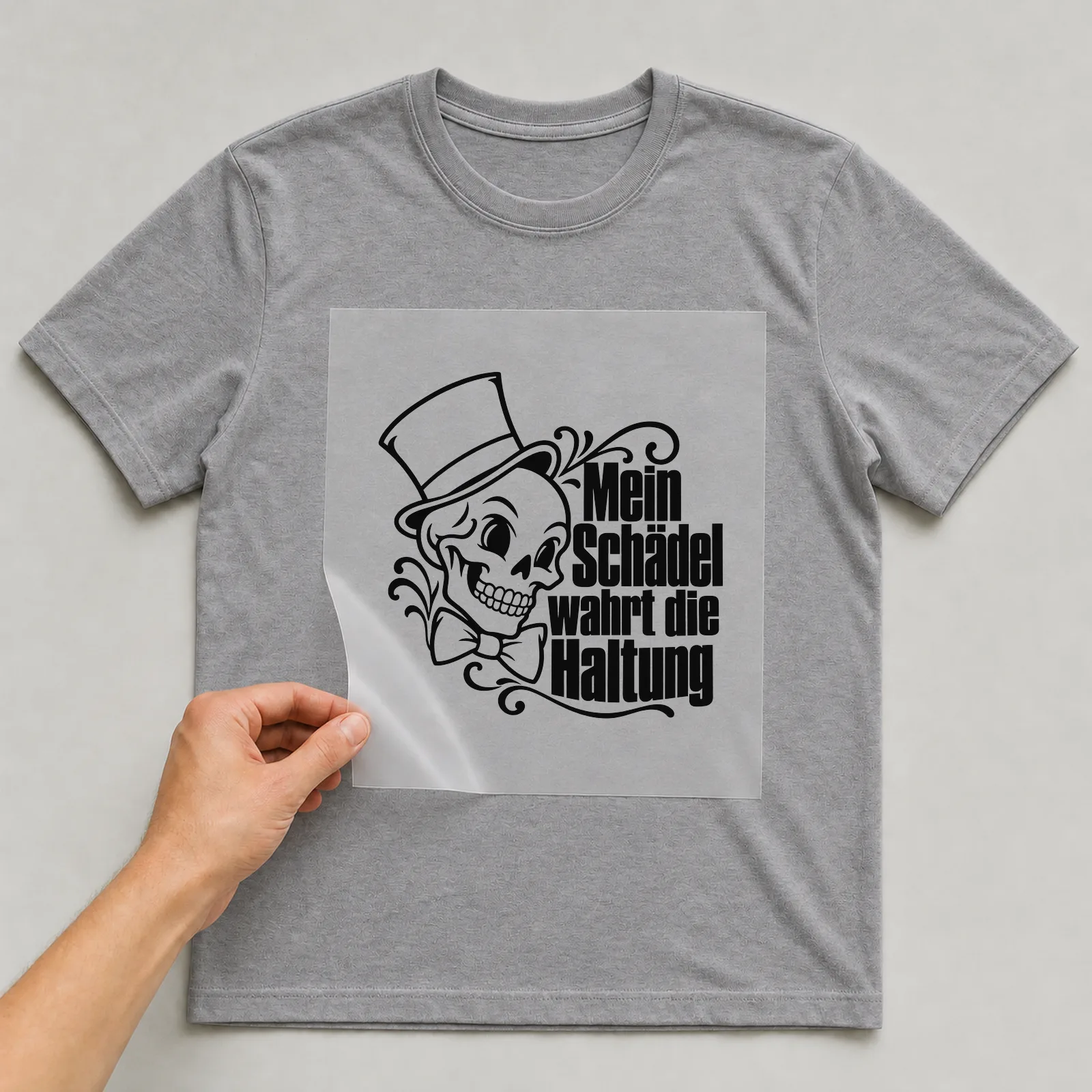 Bügelbild „Mein Schädel wahrt die Haltung“ auf grauem T-Shirt, Folie wird aufgelegt