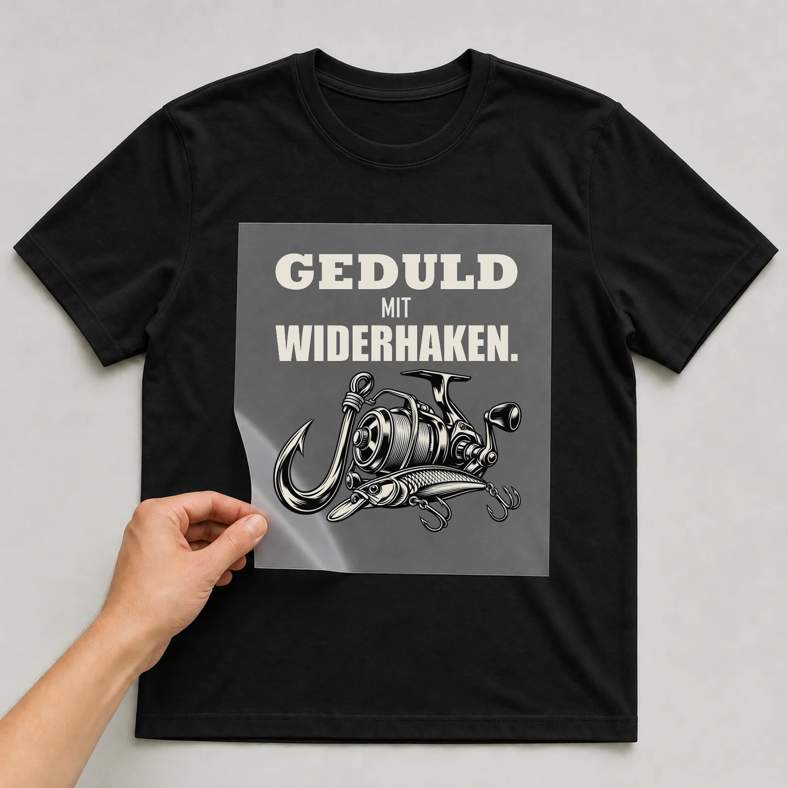 Bügelbild „Geduld mit Widerhaken“ auf schwarzem T-Shirt, Folie wird aufgelegt