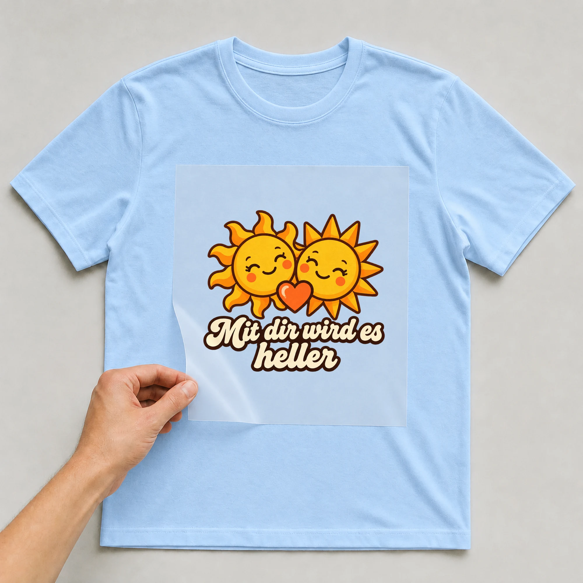 Bügelbild „Mit dir wird es heller“ auf hellblauem T-Shirt, Folie wird aufgelegt