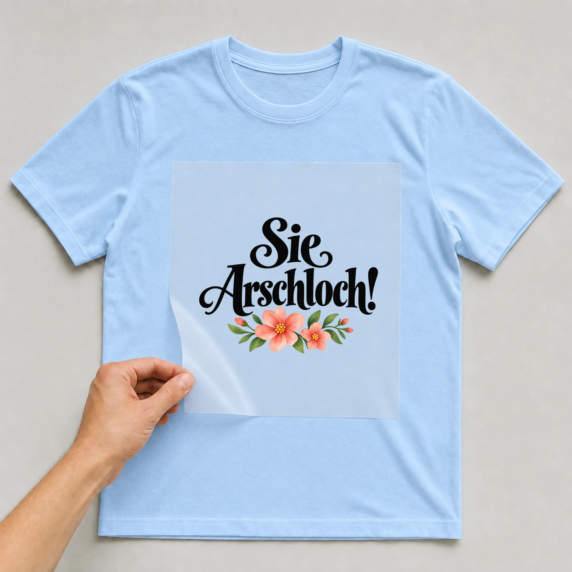 Bügelbild „Sie Ar**hloch!“ auf babyblauem T-Shirt, Folie wird aufgelegt