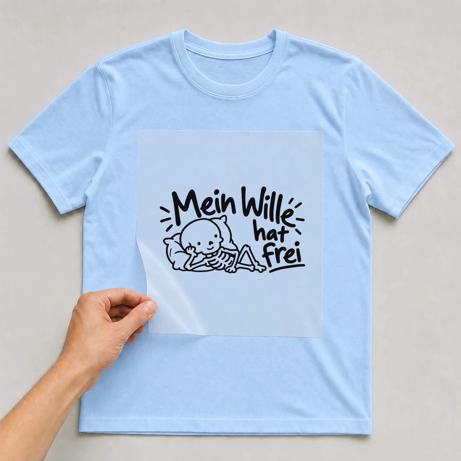 Bügelbild „Mein Wille hat frei“ auf hellblauem T-Shirt, Folie wird aufgelegt