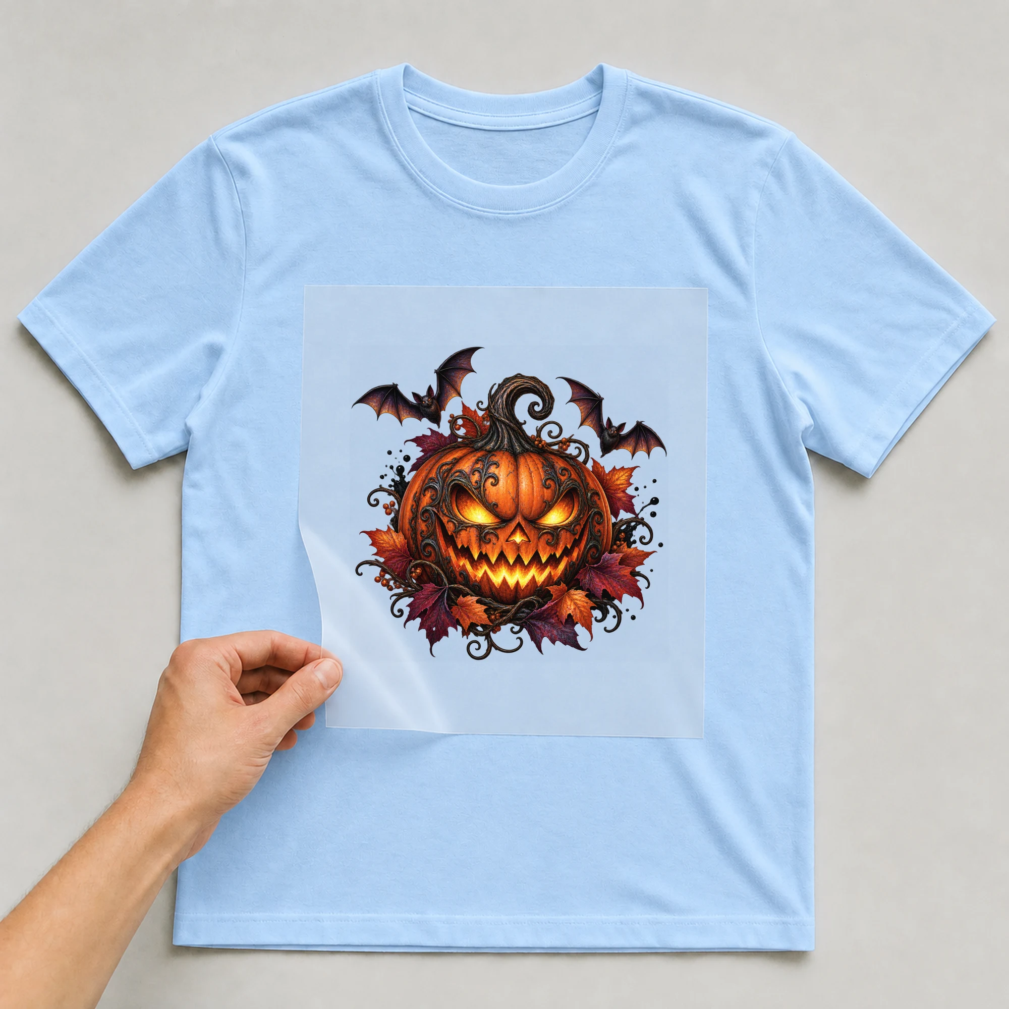 Bügelbild „Gruselkürbis mit Fledermäusen“ auf babyblauem T-Shirt, Folie wird aufgelegt
