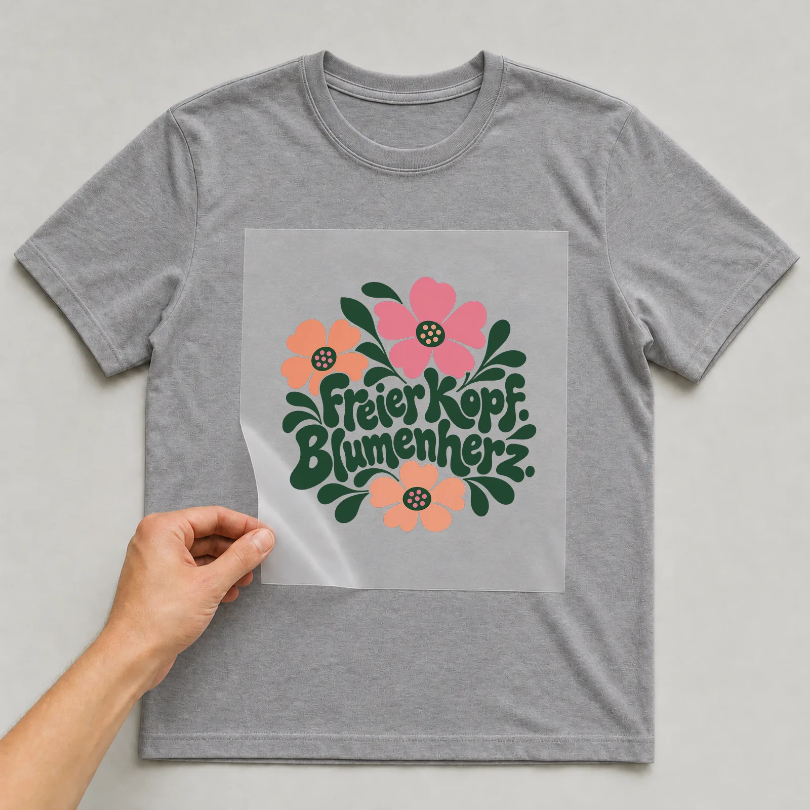 Bügelbild „Freier Kopf. Blumenherz.“ auf grauem T-Shirt, Folie wird aufgelegt