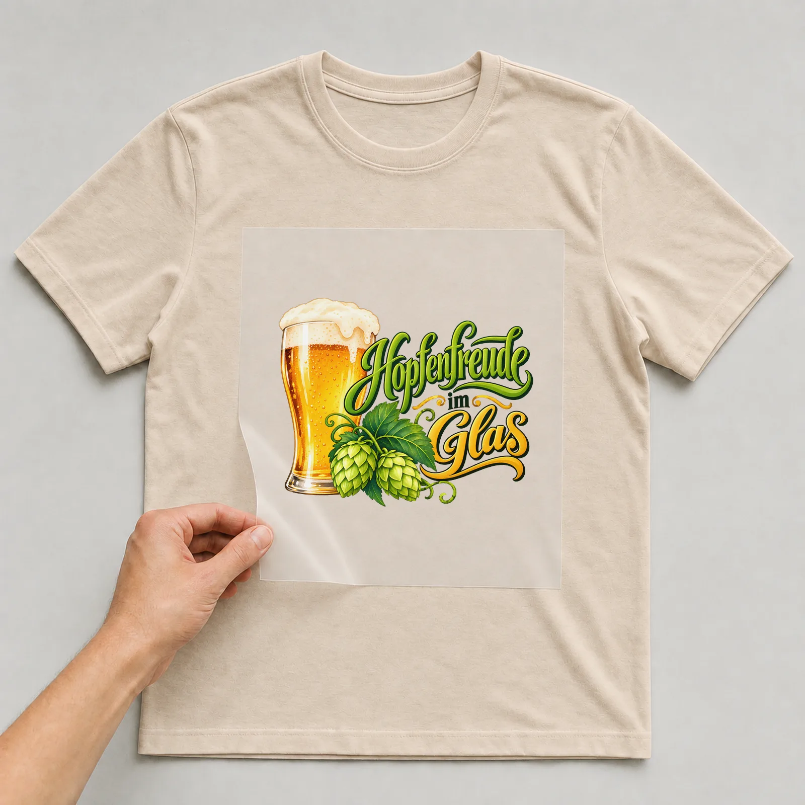 Bügelbild „Hopfenfreude im Glas“ auf beigem T-Shirt, Folie wird aufgelegt