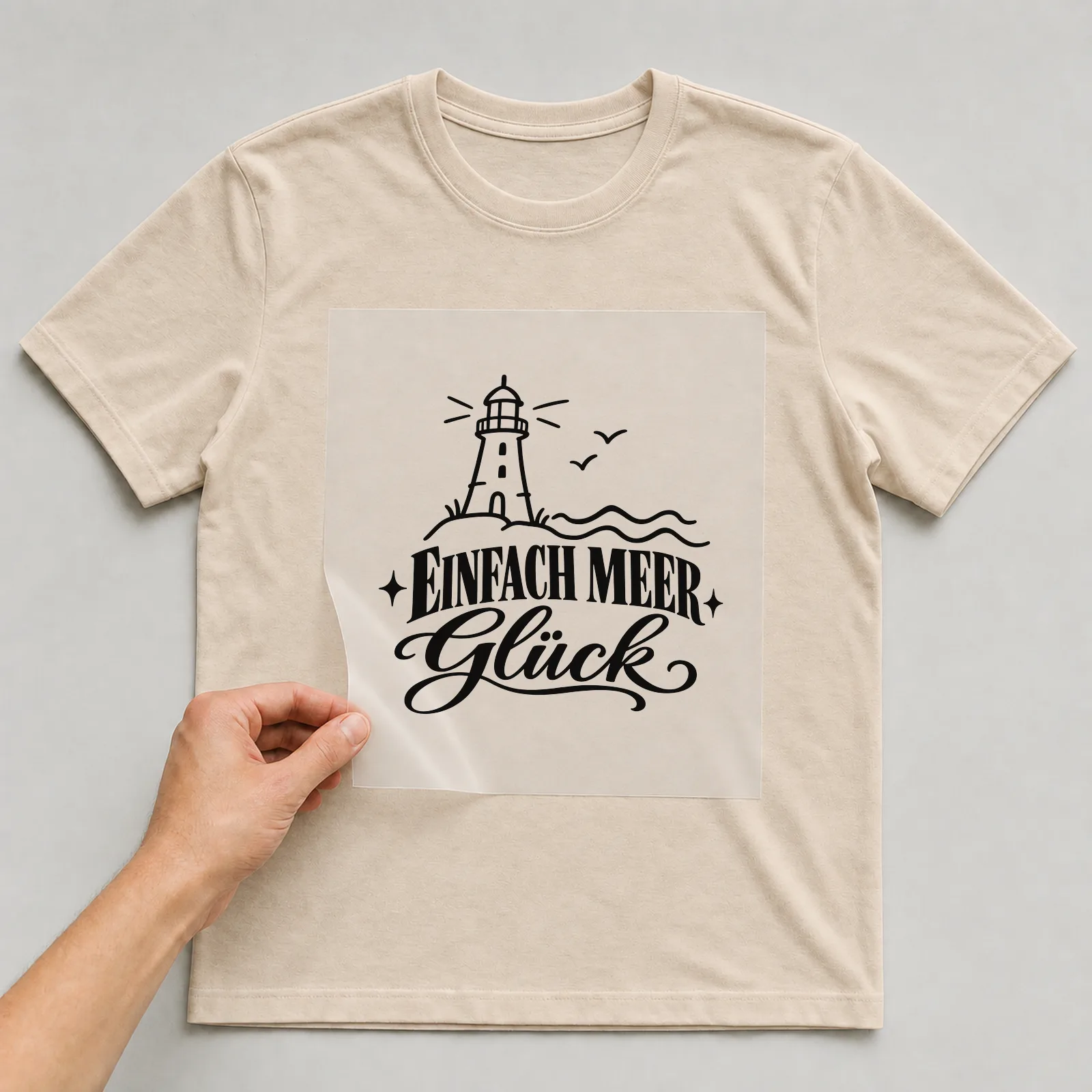 Bügelbild „Einfach Meer Glück“ auf beigem T-Shirt, Folie wird aufgelegt
