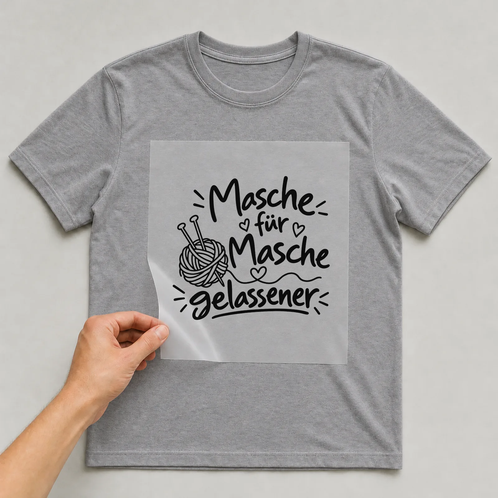 Bügelbild „Masche für Masche gelassener“ auf grauem T-Shirt, Folie wird aufgelegt