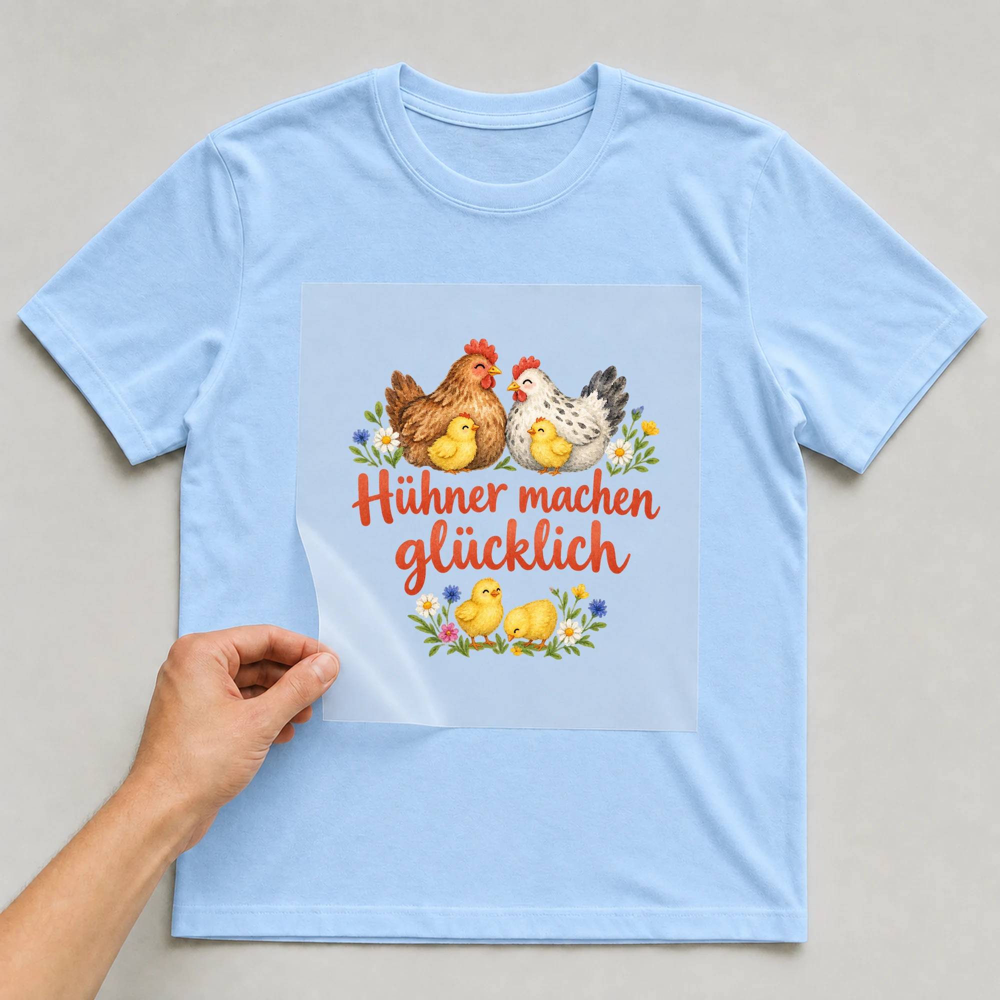 Bügelbild „Hühner machen glücklich“ auf babyblauem T-Shirt, Folie wird aufgelegt
