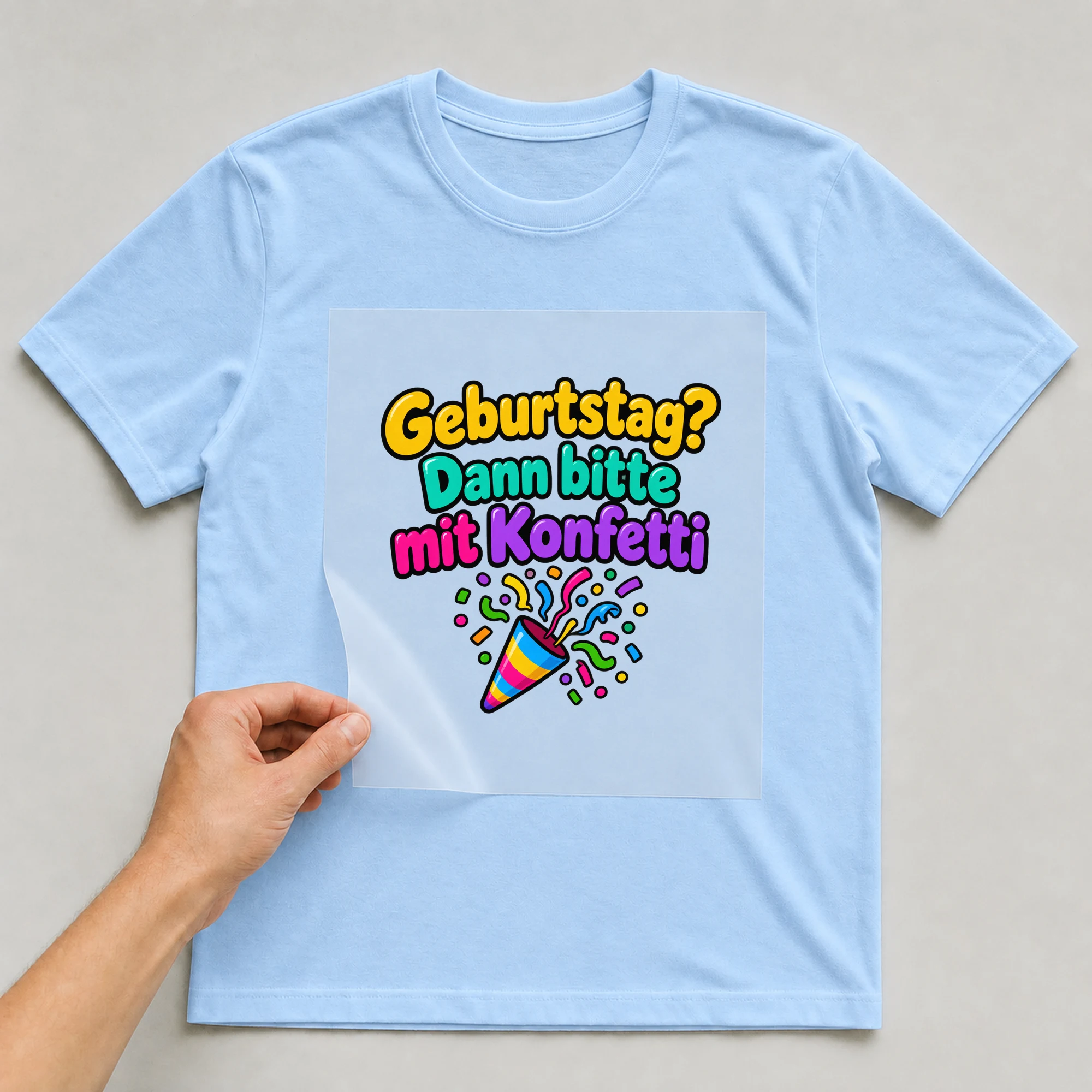Bügelbild „Geburtstag dann bitte mit konfetti“ auf babyblauem T-Shirt, Folie wird aufgelegt