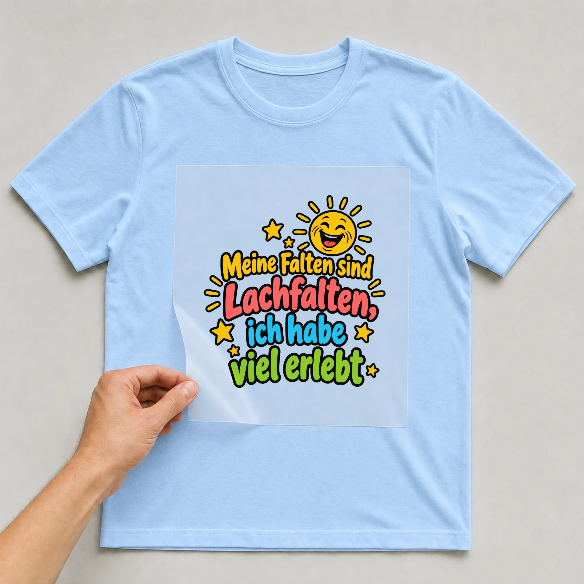 Bügelbild „Meine Falten sind Lachfalten, ich habe viel erlebt“ auf babyblauem T-Shirt, Folie wird aufgelegt