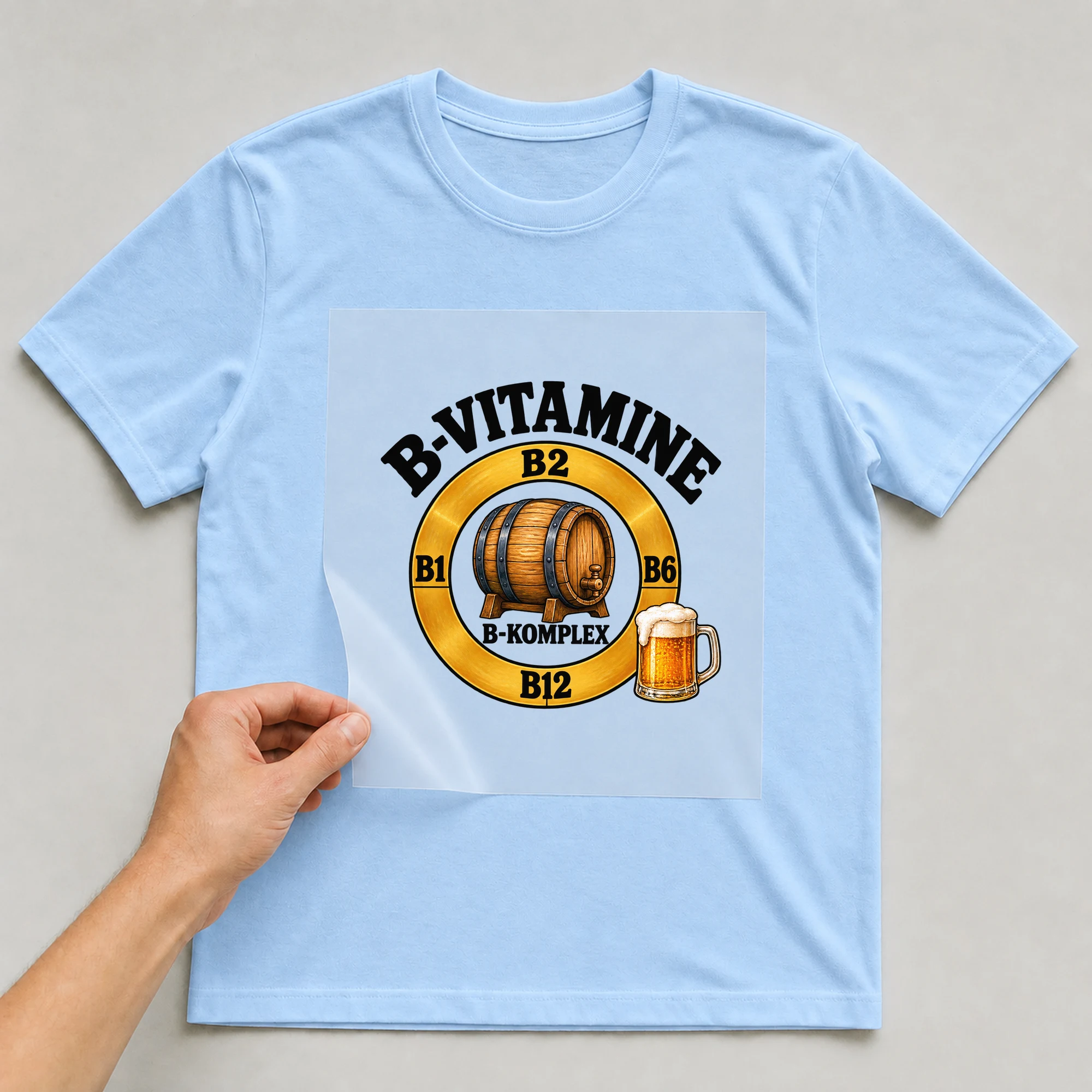 Bügelbild „B-vitamine B1 B2 B6 B12 B-komplex“ auf babyblauem T-Shirt, Folie wird aufgelegt