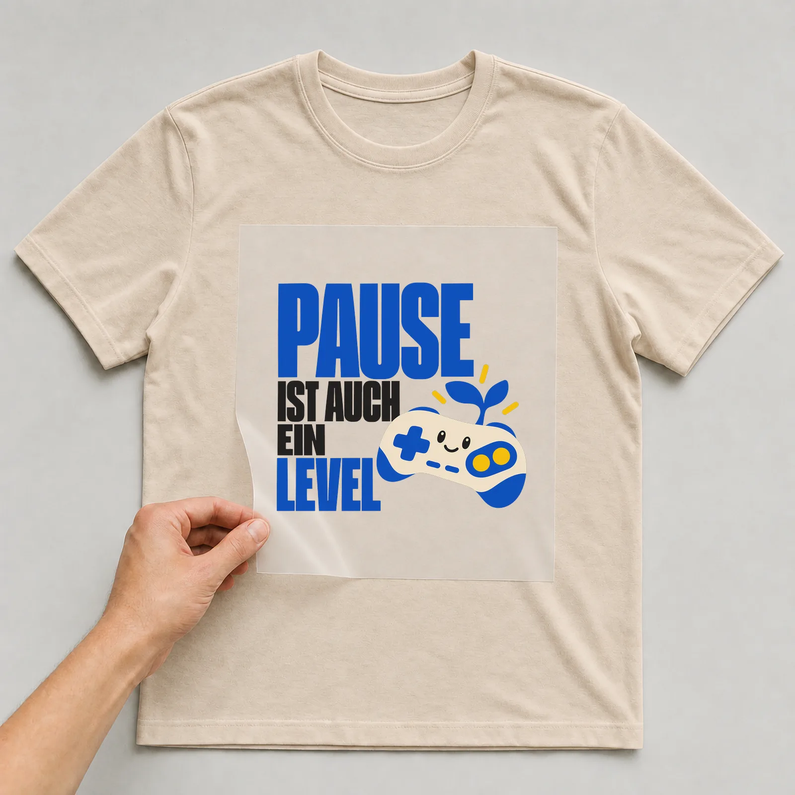 Bügelbild „Pause ist auch ein Level“ (organischen Formen) auf beigem T-Shirt, Folie wird aufgelegt