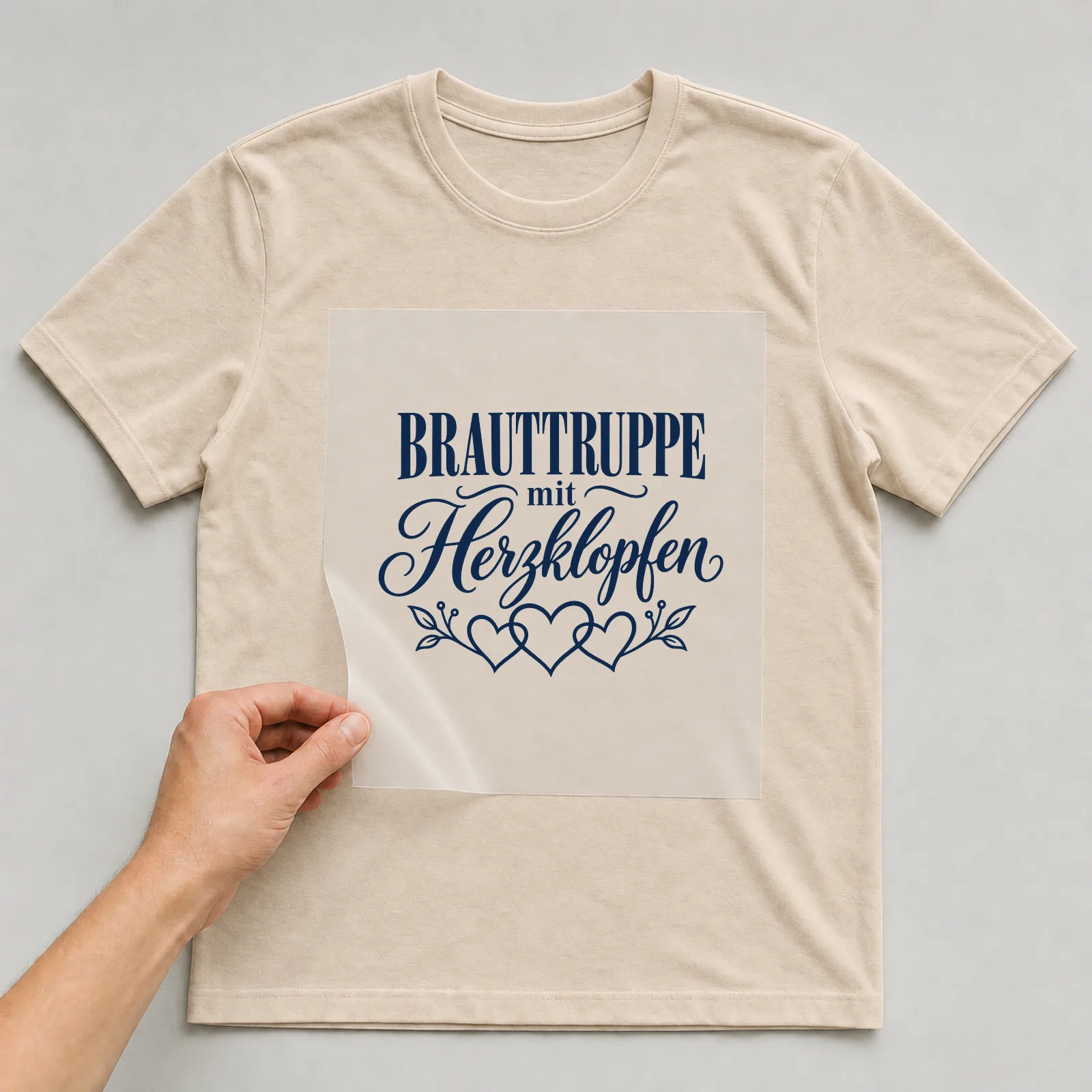 Bügelbild „Brauttruppe mit Herzklopfen“ auf beigem T-Shirt, Folie wird aufgelegt