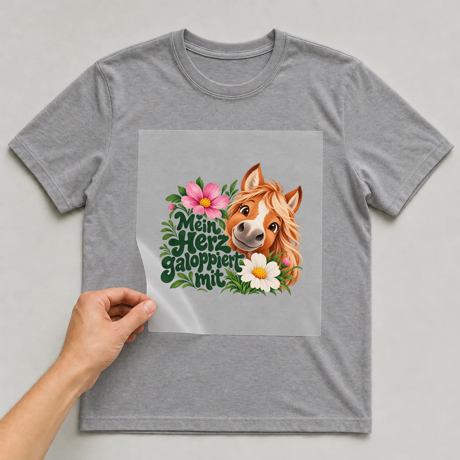 Bügelbild „Mein Herz galoppiert mit“ auf grauem T-Shirt, Folie wird aufgelegt