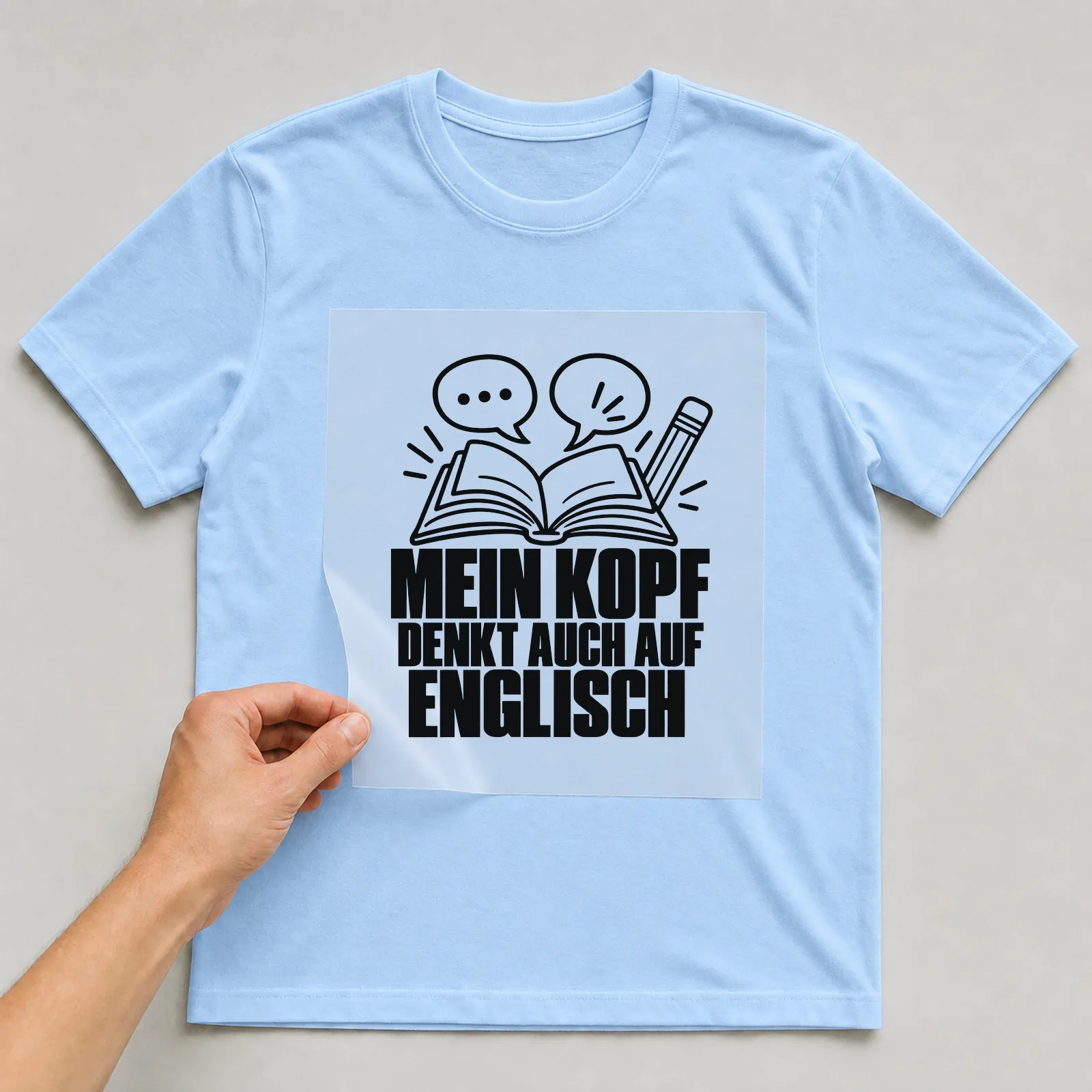Bügelbild „Mein Kopf denkt auch auf Englisch“ auf hellblauem T-Shirt, Folie wird aufgelegt