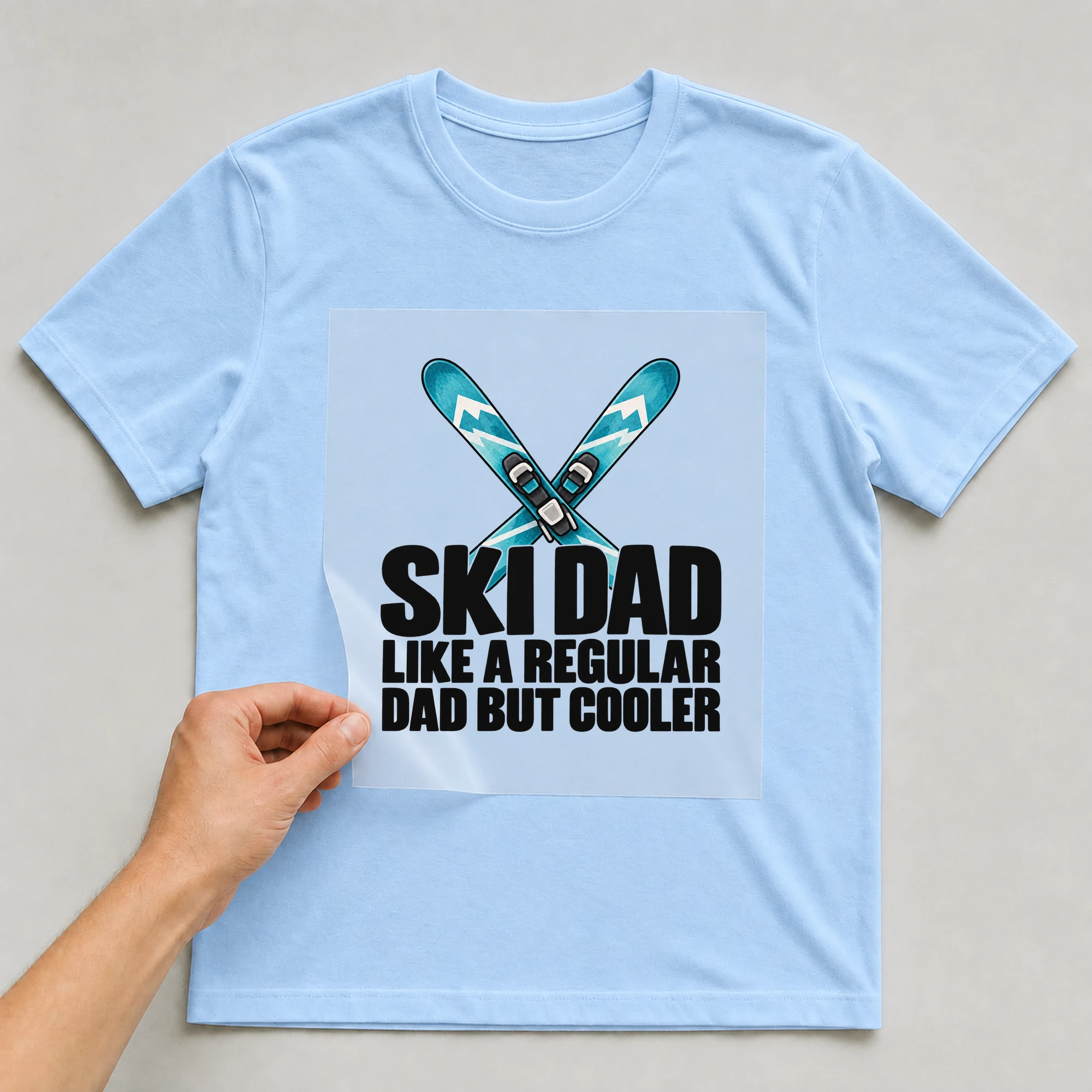 Bügelbild „Ski Dad Like A Regular Dad But Cooler“ auf babyblauem T-Shirt, Folie wird aufgelegt