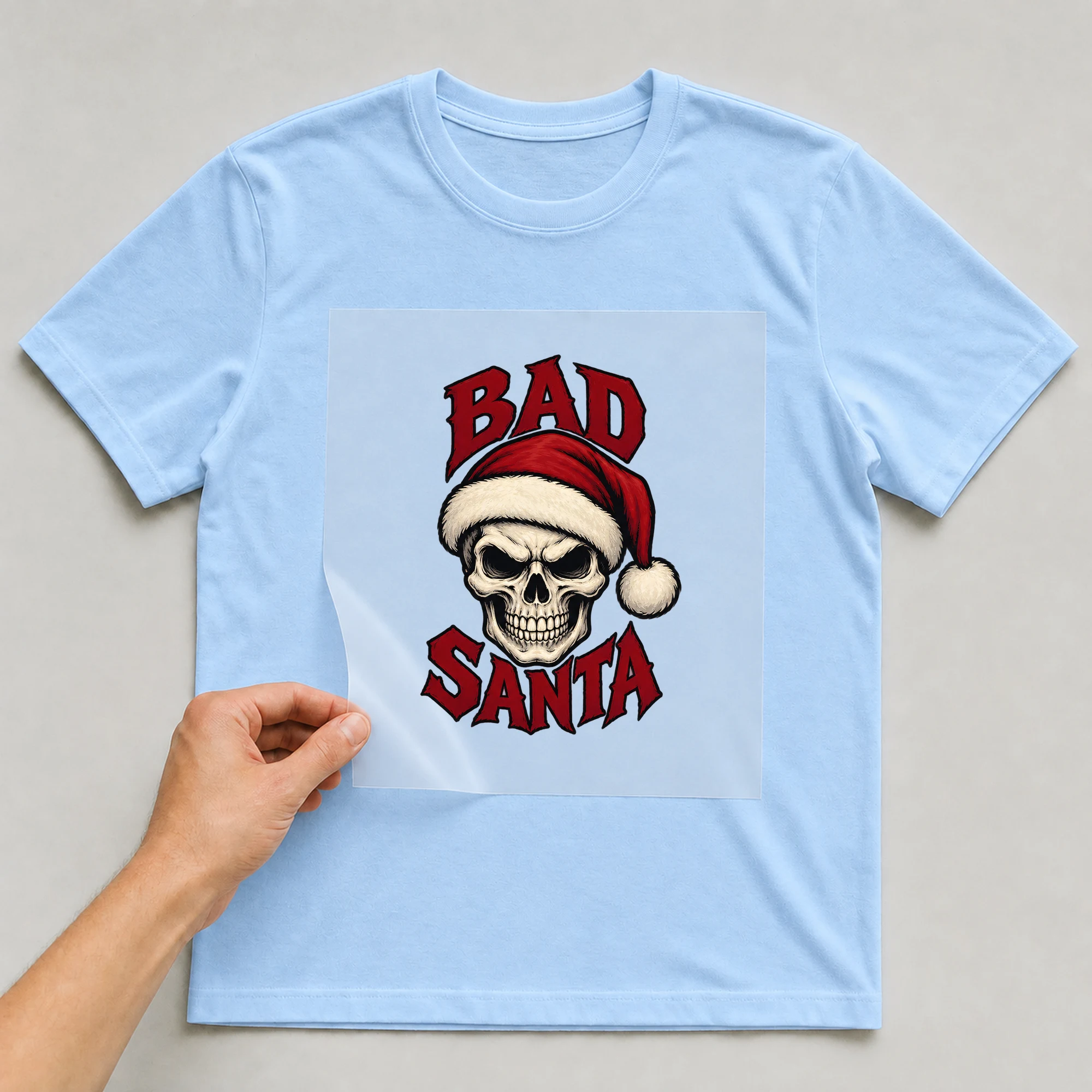 Bügelbild „Bad Santa“ auf babyblauem T-Shirt, Folie wird aufgelegt