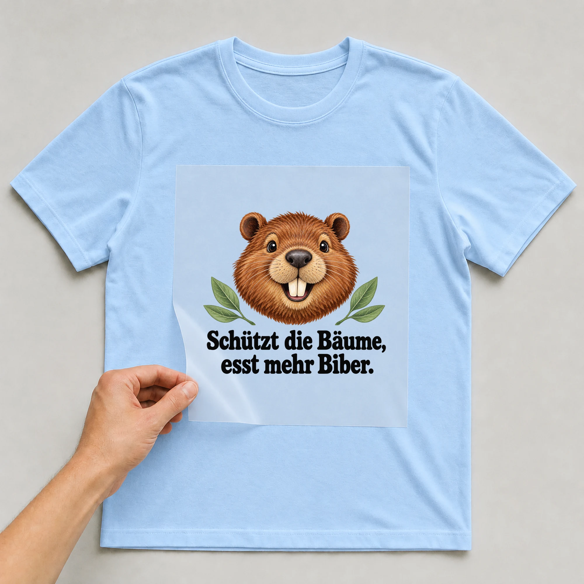 Bügelbild „Schützt die Bäume, esst mehr Biber.“ auf babyblauem T-Shirt, Folie wird aufgelegt