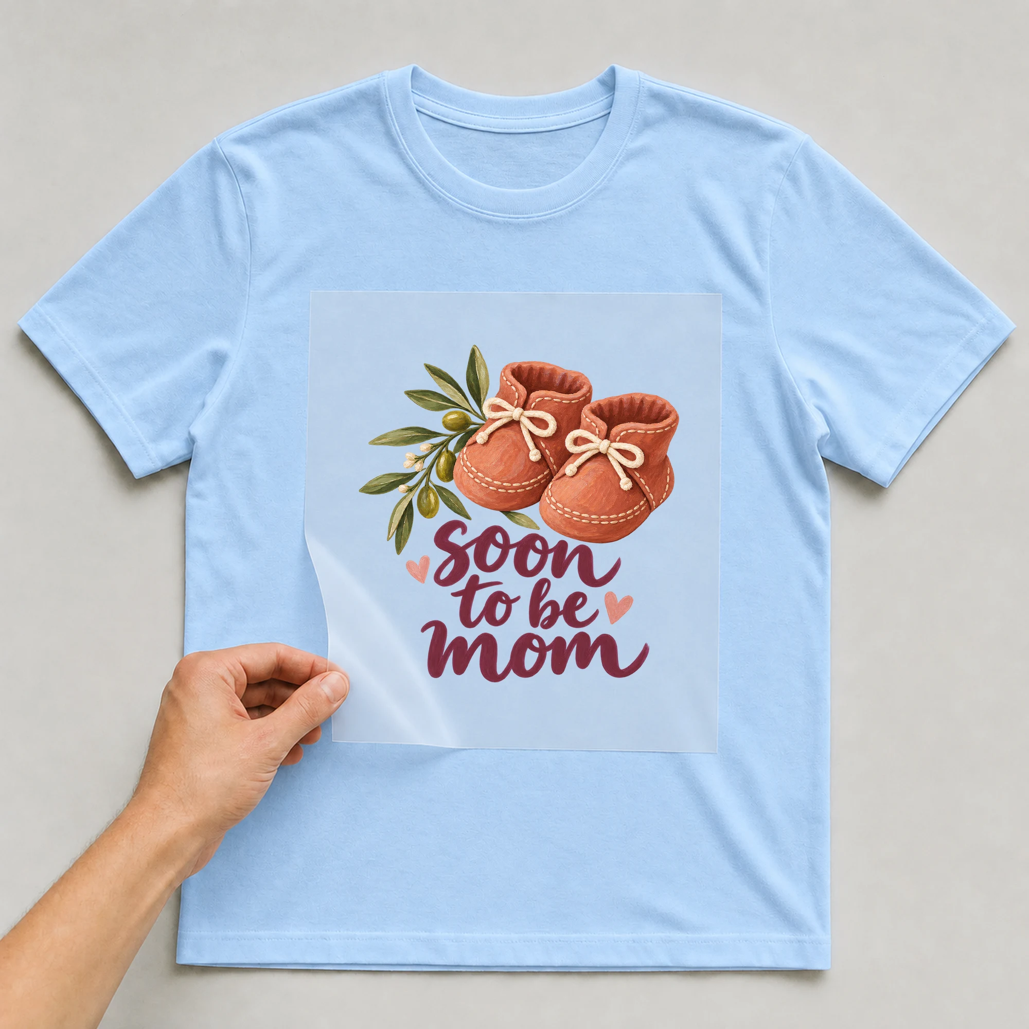 Bügelbild „soon to be mom“ auf babyblauem T-Shirt, Folie wird aufgelegt