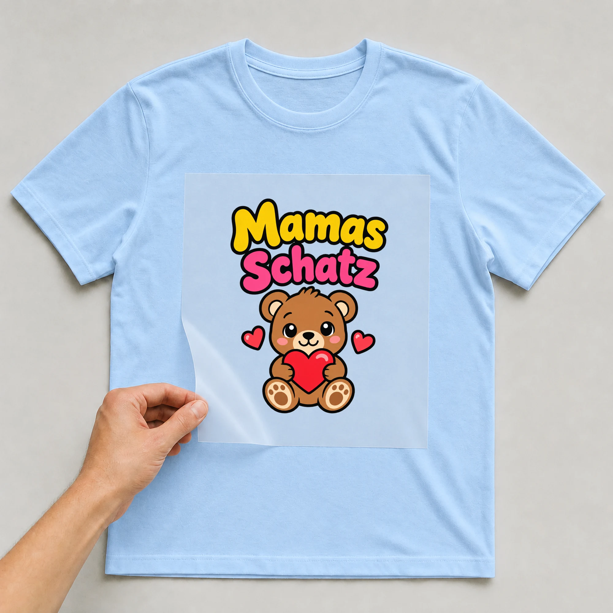 Bügelbild „Mamas Schatz“ auf babyblauem T-Shirt, Folie wird aufgelegt