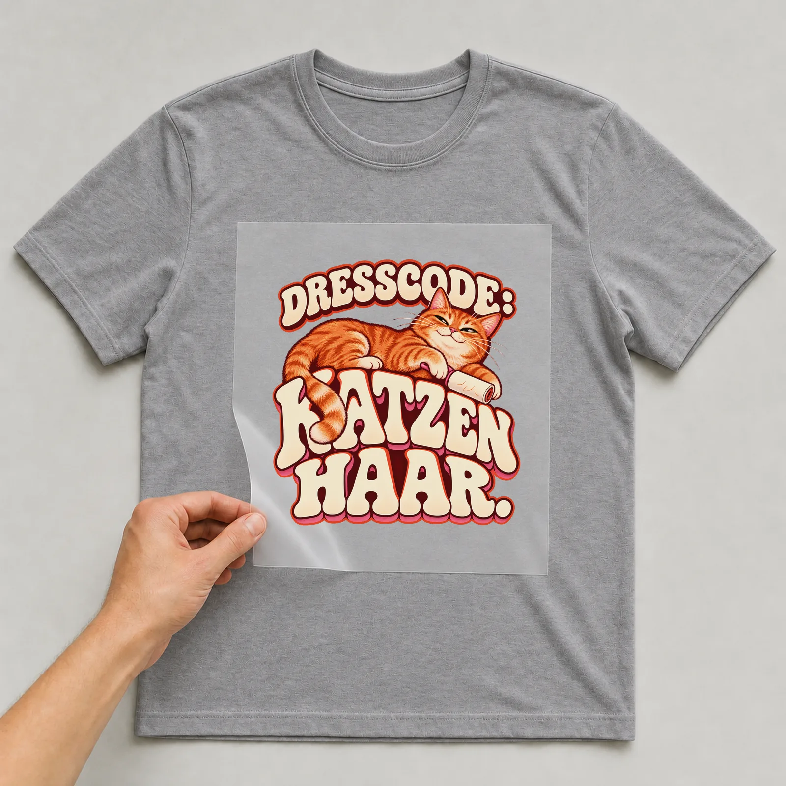 Bügelbild „Dresscode: Katzenhaar“ auf grauem T-Shirt, Folie wird aufgelegt