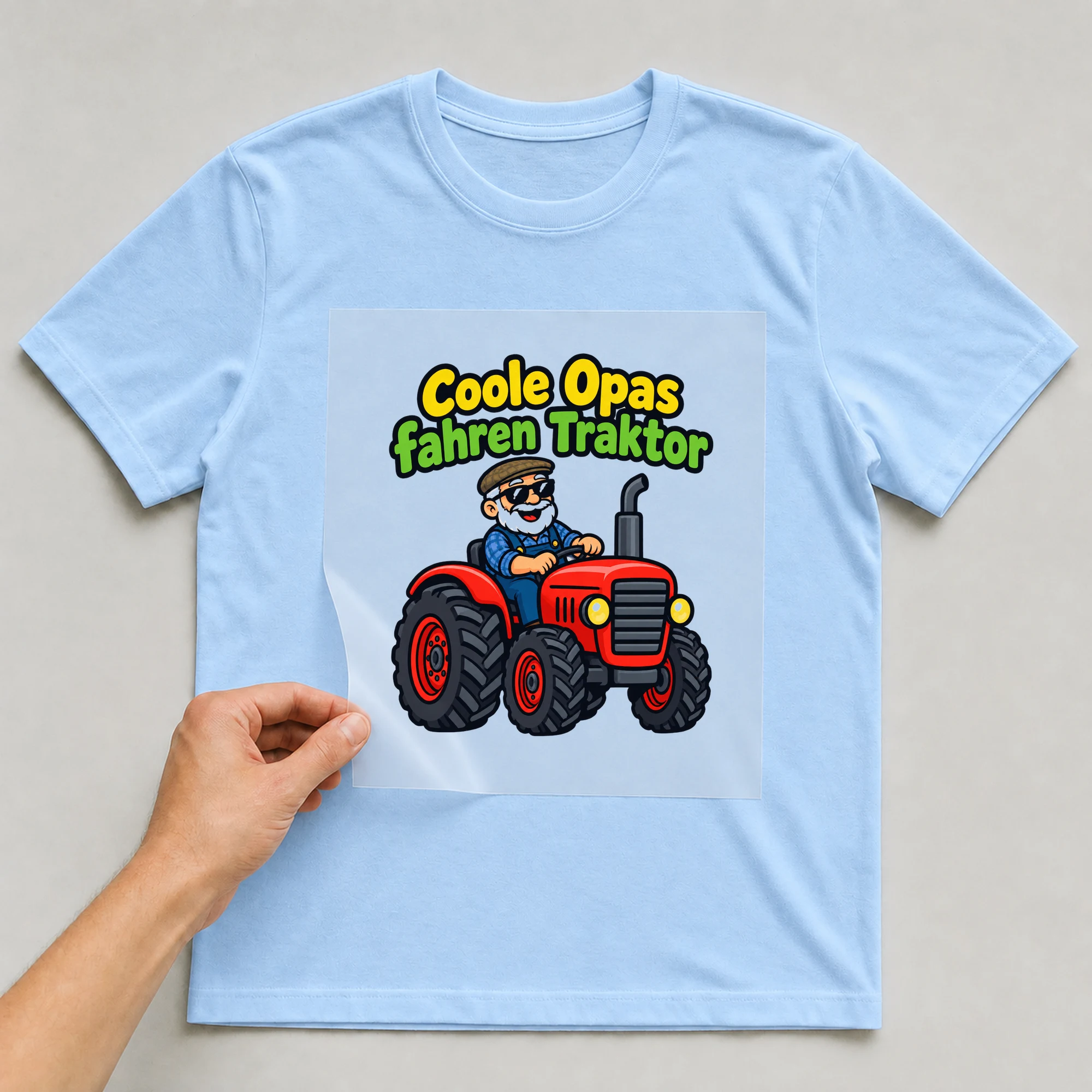 Bügelbild „Coole Opas fahren Traktor“ auf babyblauem T-Shirt, Folie wird aufgelegt