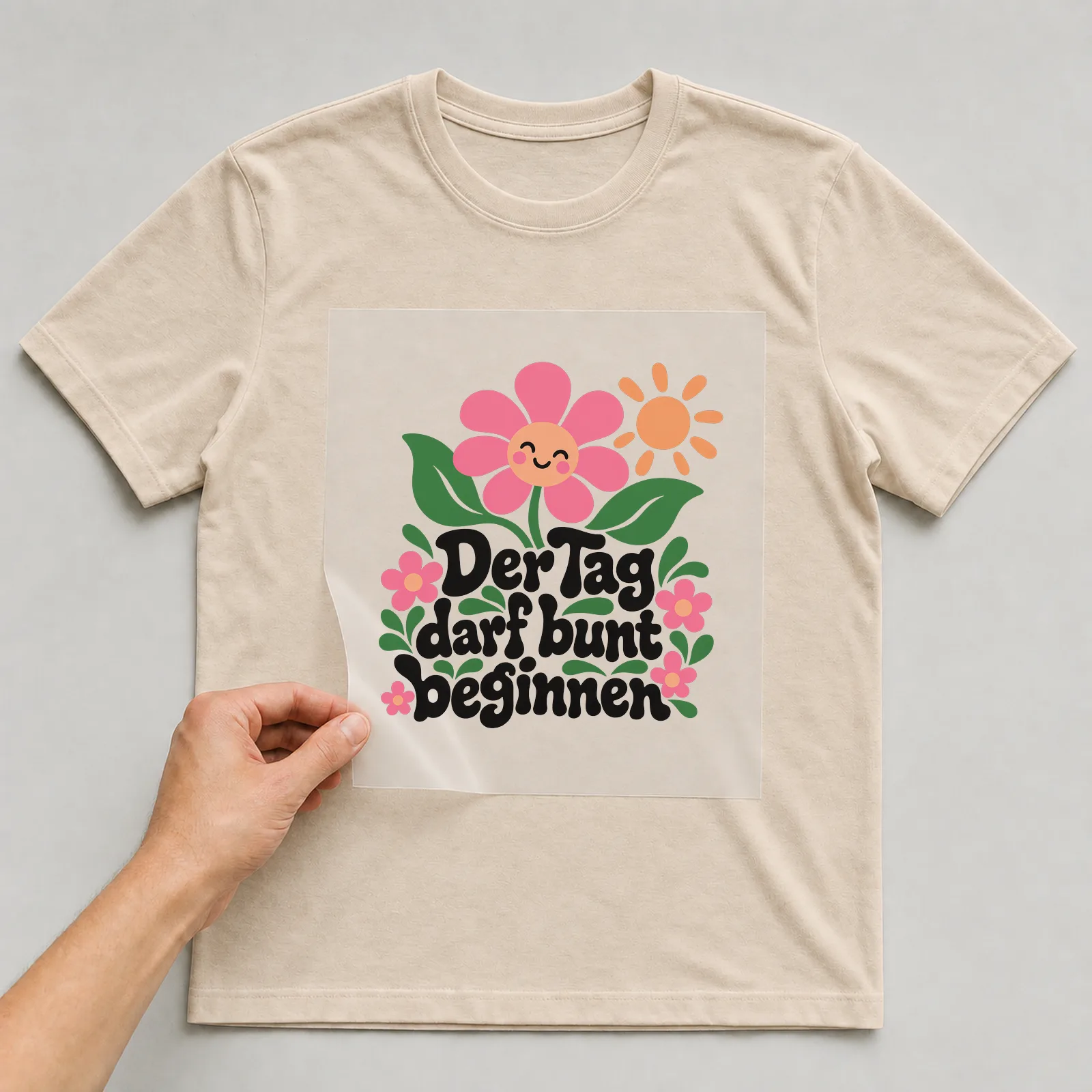 Bügelbild „Der Tag darf bunt beginnen“ auf beigem T-Shirt, Folie wird aufgelegt