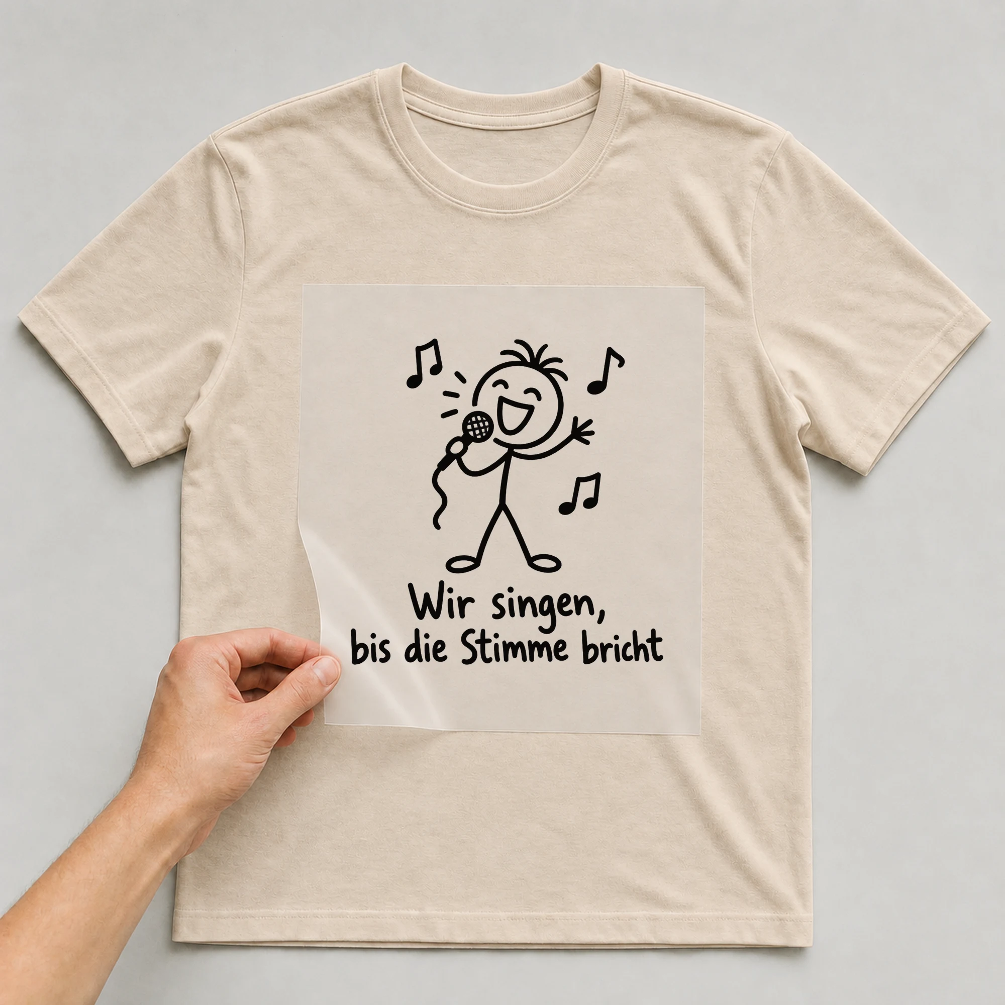 Bügelbild „Wir singen, bis die Stimme bricht“ auf beigem T-Shirt, Folie wird aufgelegt