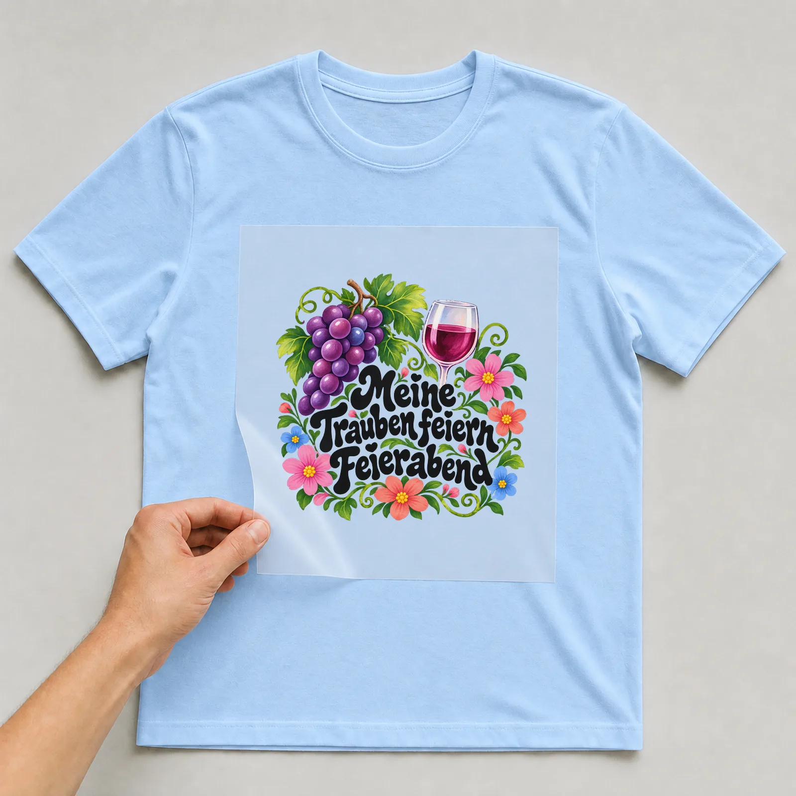 Bügelbild „Meine Trauben feiern Feierabend“ auf hellblauem T-Shirt, Folie wird aufgelegt