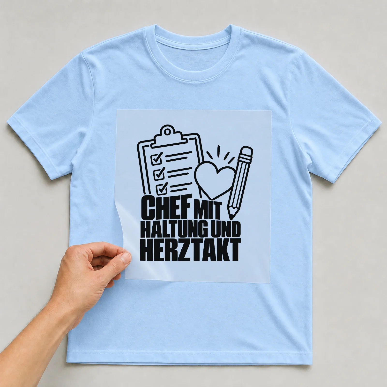 Bügelbild „Chef mit Haltung und Herztakt“ auf hellblauem T-Shirt, Folie wird aufgelegt