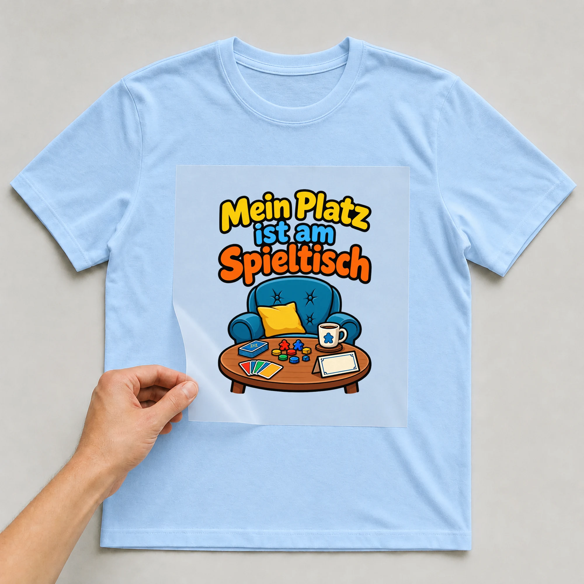Bügelbild „Mein Platz ist am Spieltisch“ auf babyblauem T-Shirt, Folie wird aufgelegt