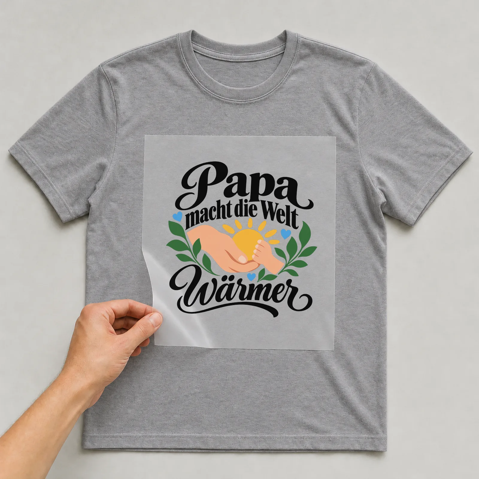 Bügelbild „Papa macht die Welt wärmer“ auf grauem T-Shirt, Folie wird aufgelegt