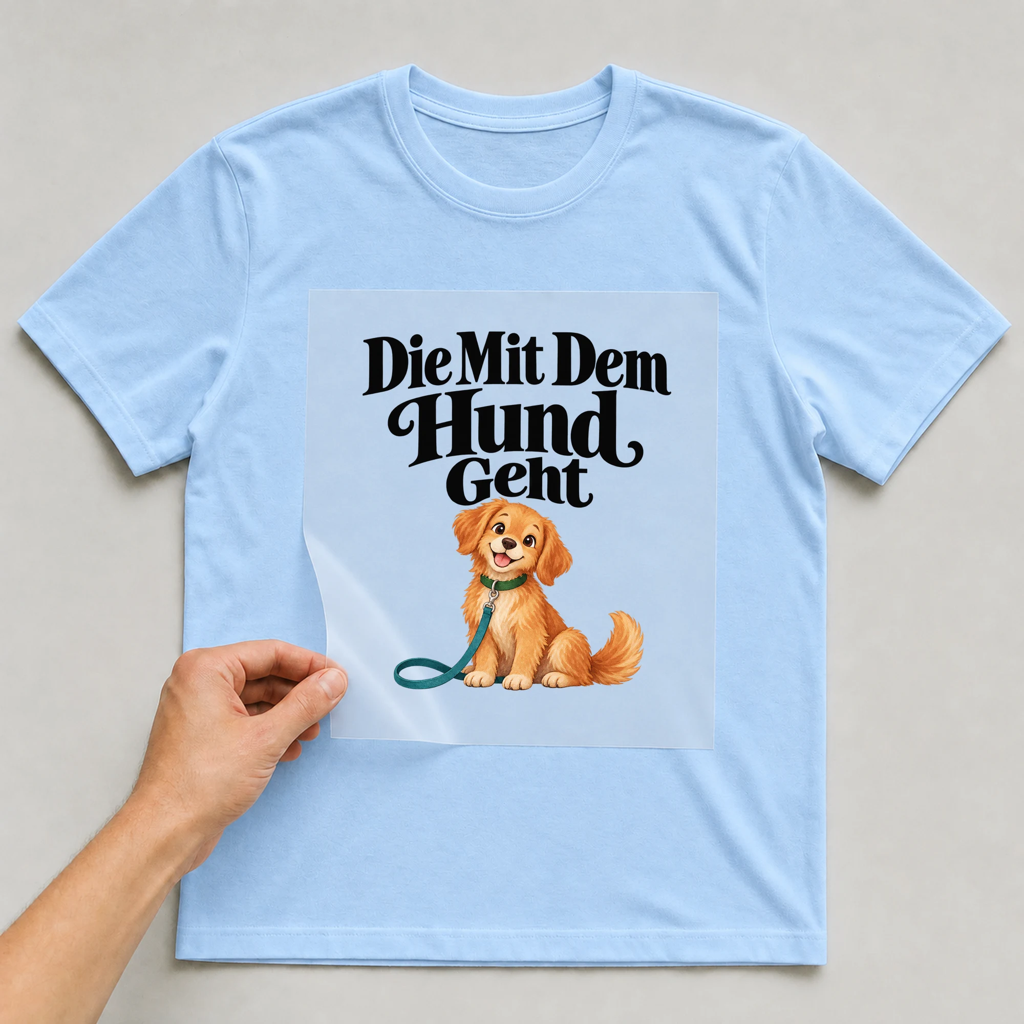 Bügelbild „Die Mit Dem Hund Geht“ auf babyblauem T-Shirt, Folie wird aufgelegt