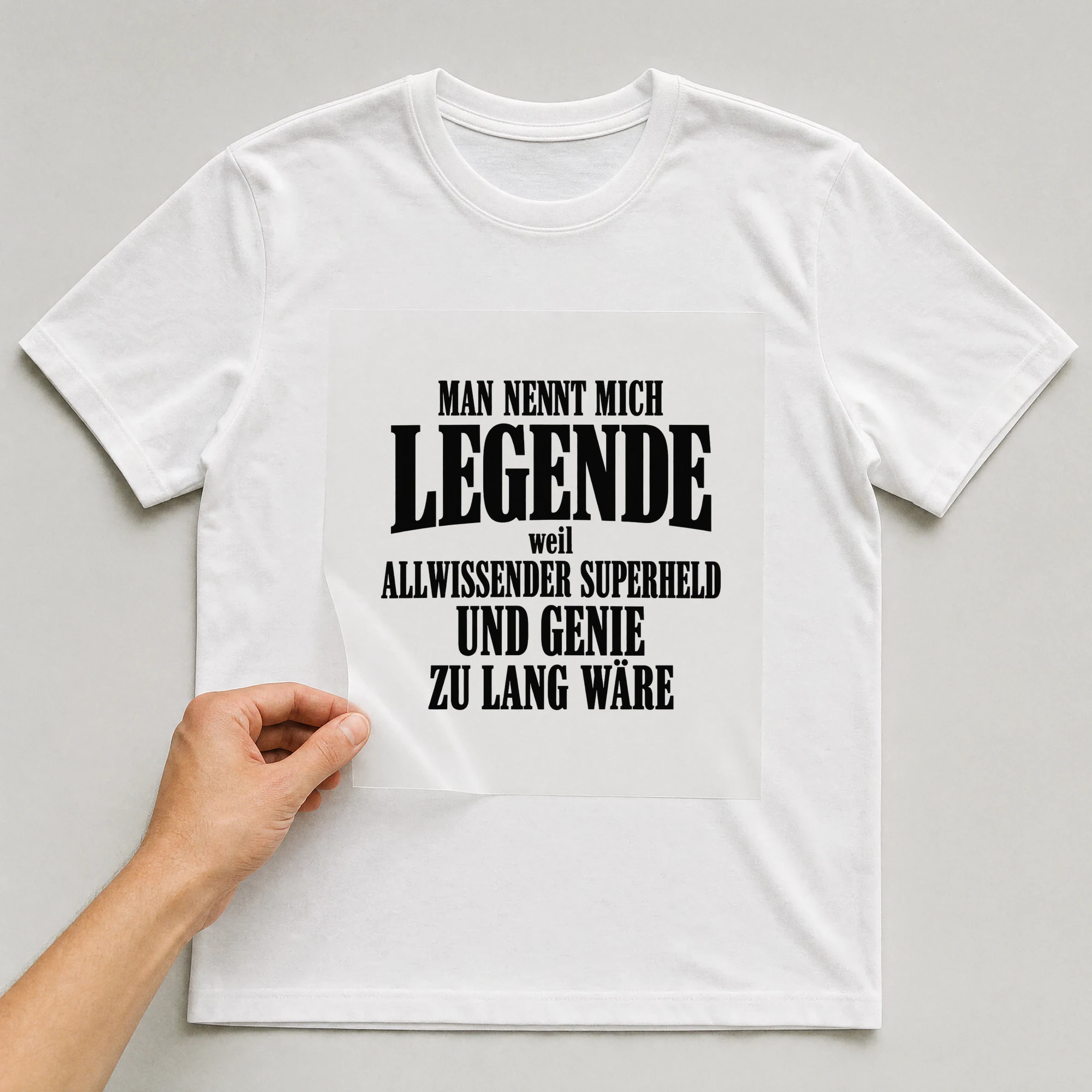 Bügelbild „Man nennt mich Legende, weil Allwissender Superheld und Genie zu lang wäre“ auf weißem T-Shirt, Folie wird aufgelegt