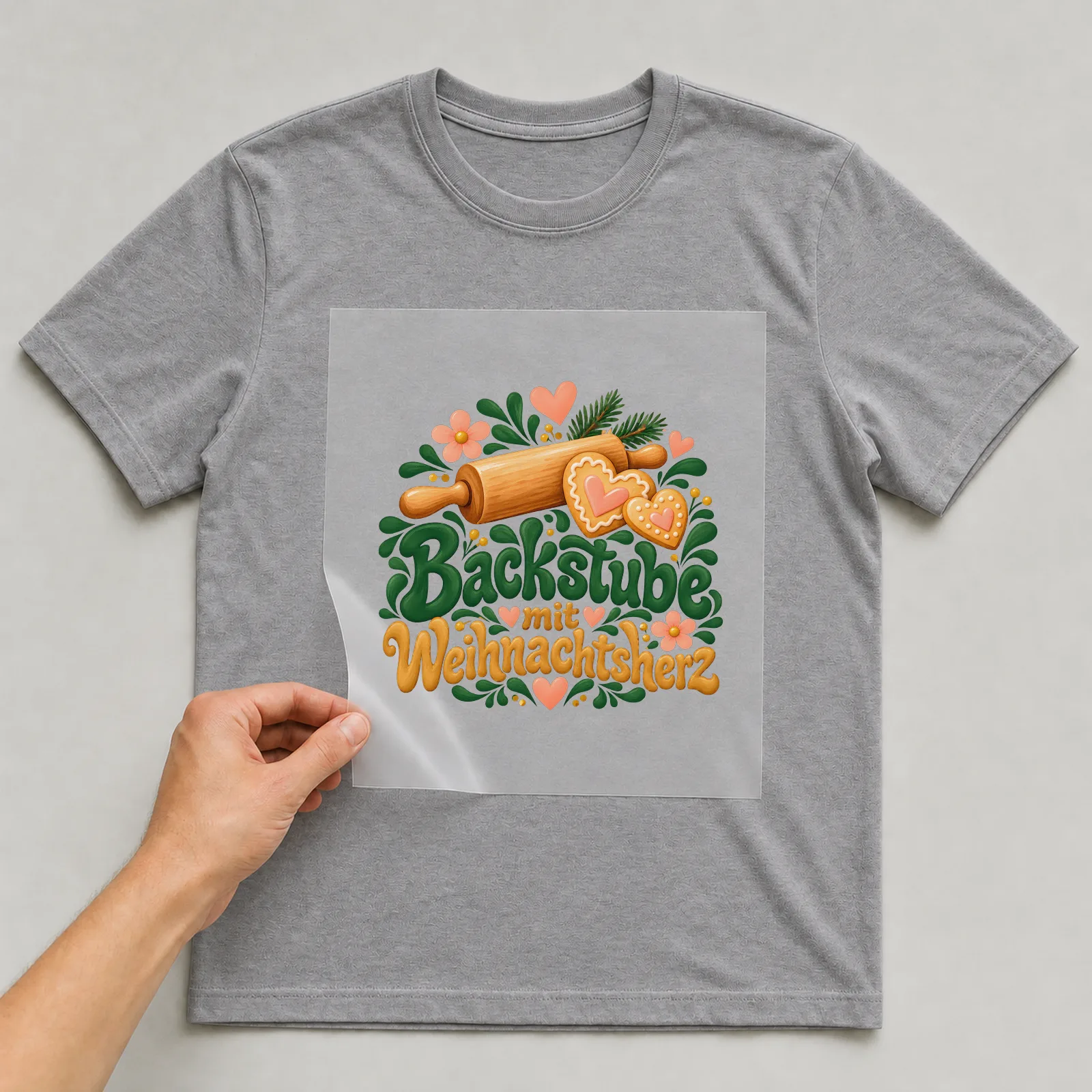 Bügelbild „Backstube mit Weihnachtsherz“ auf grauem T-Shirt, Folie wird aufgelegt
