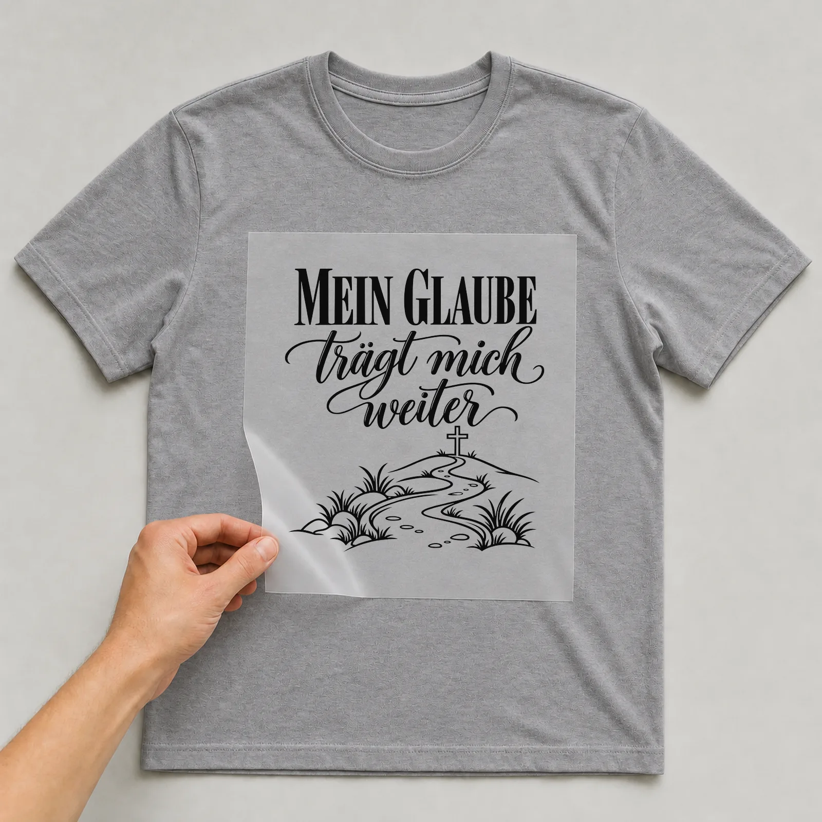 Bügelbild „Mein Glaube trägt mich weiter“ auf grauem T-Shirt, Folie wird aufgelegt