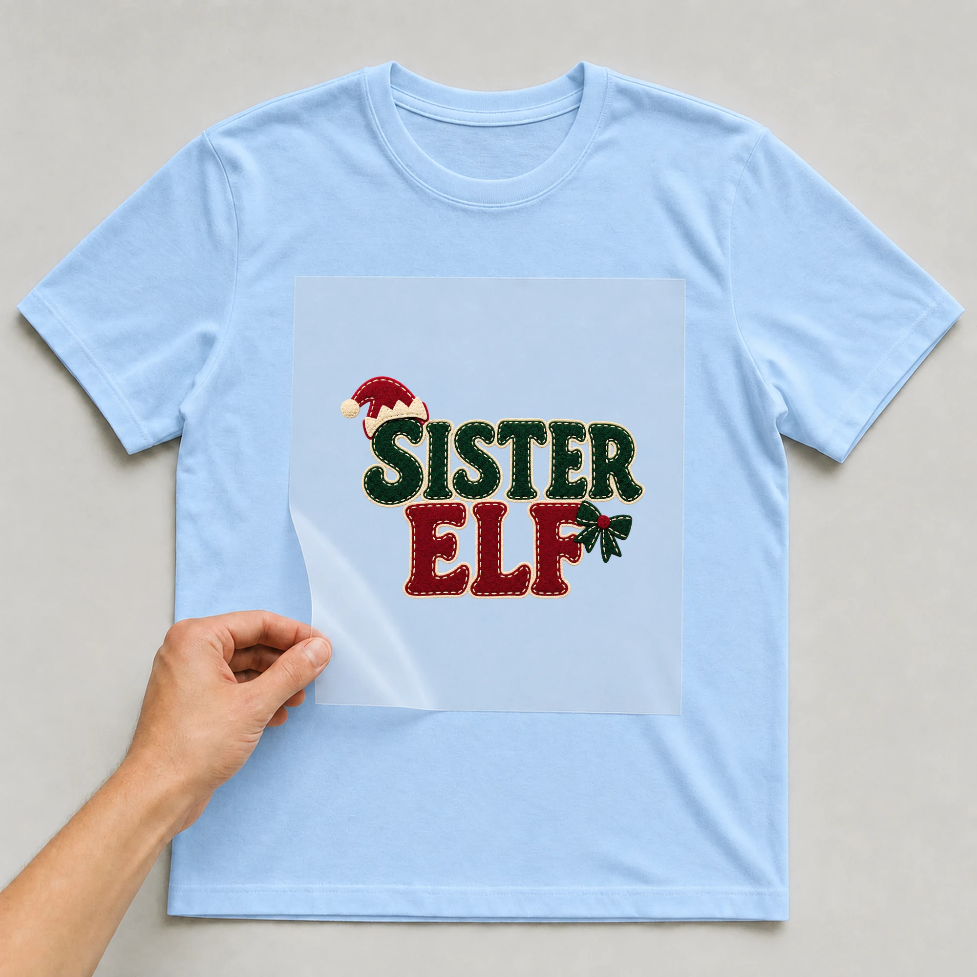 Bügelbild „Sister Elf“ auf babyblauem T-Shirt, Folie wird aufgelegt