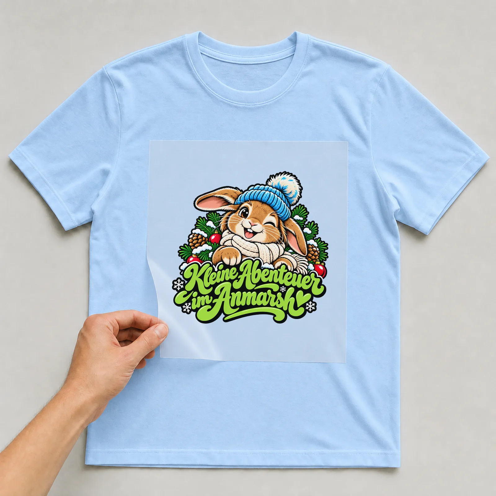 Bügelbild „Kleine Abenteuer im Anmarsch“ auf hellblauem T-Shirt, Folie wird aufgelegt