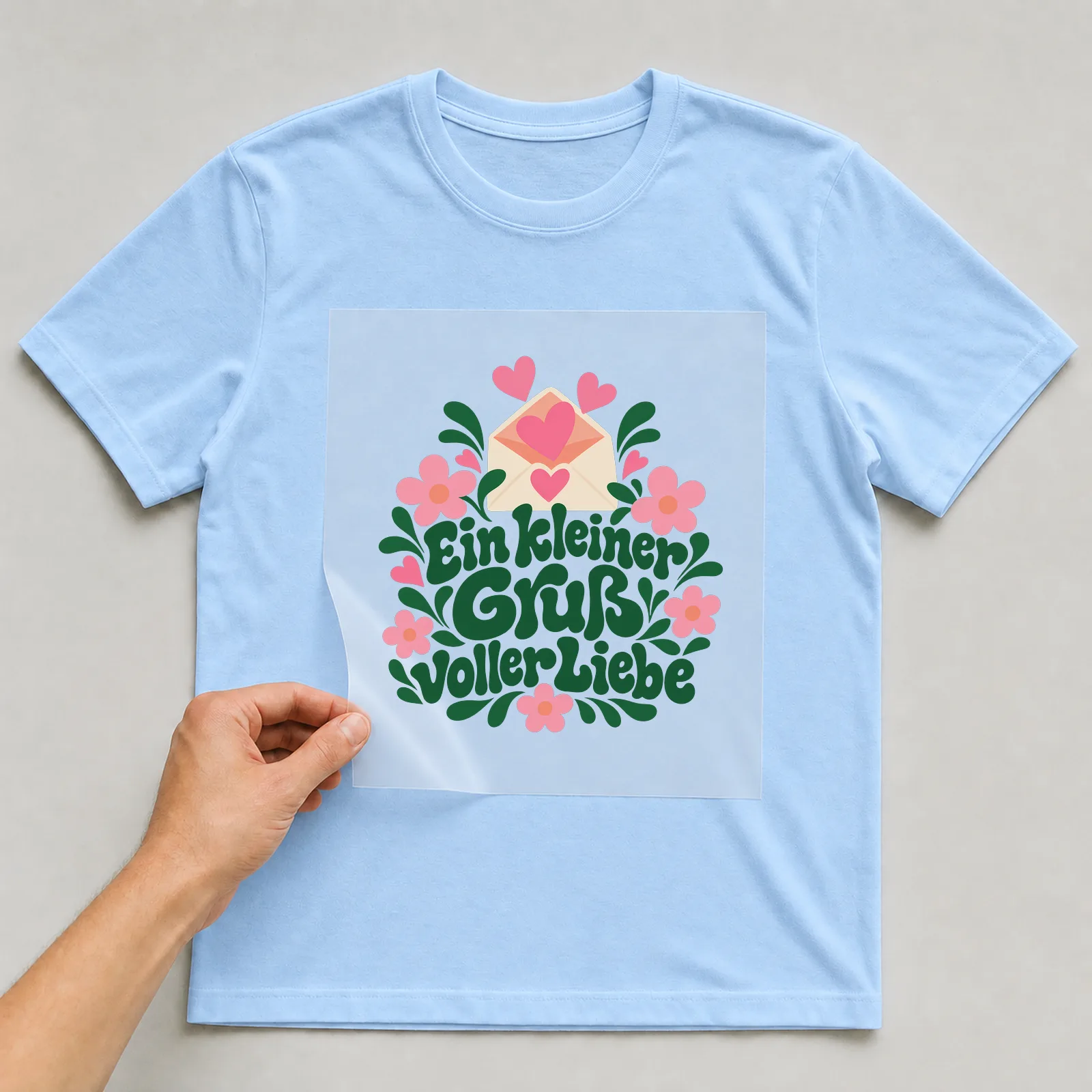 Bügelbild „Ein kleiner Gruß voller Liebe“ auf hellblauem T-Shirt, Folie wird aufgelegt