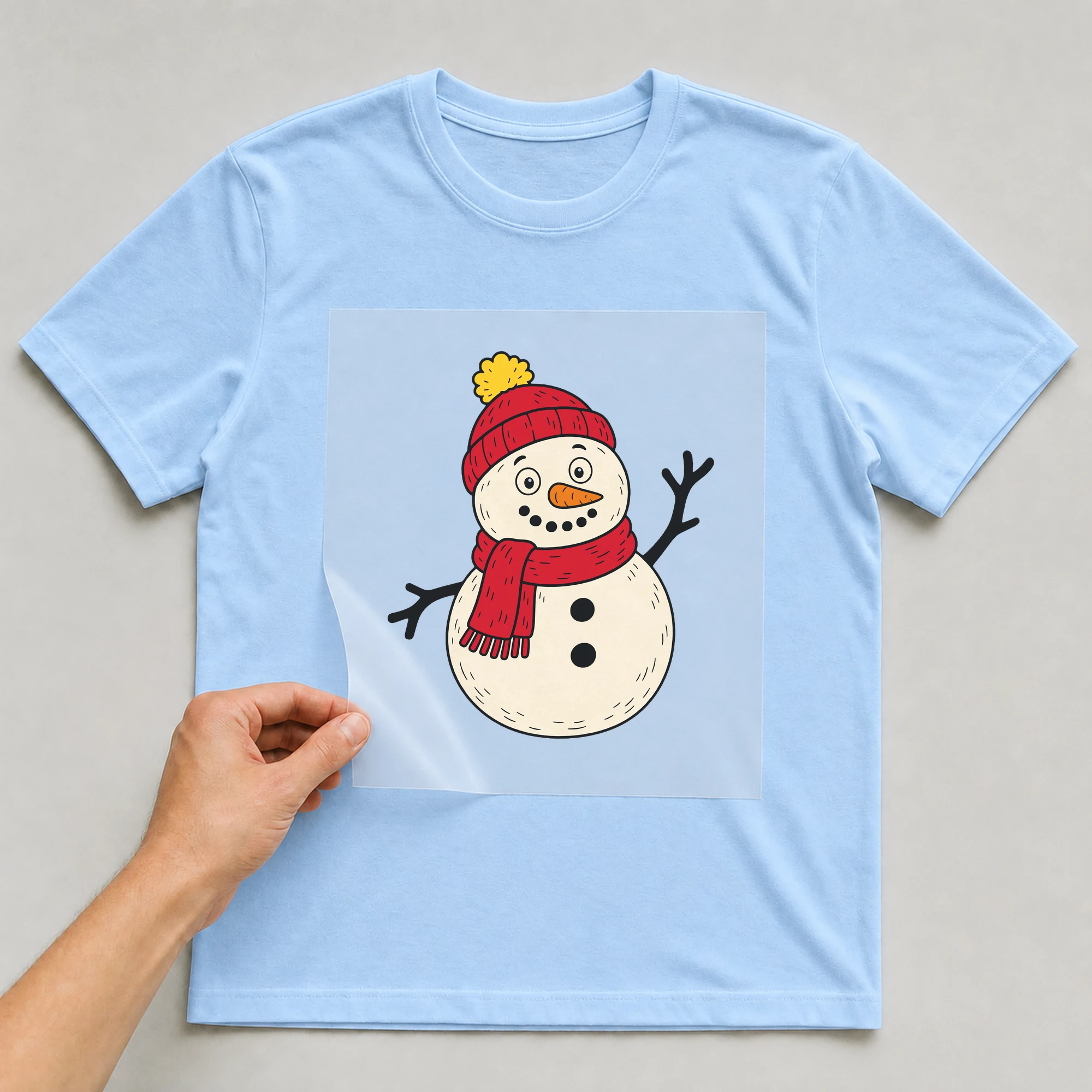 Bügelbild „Schneemann“ auf babyblauem T-Shirt, Folie wird aufgelegt