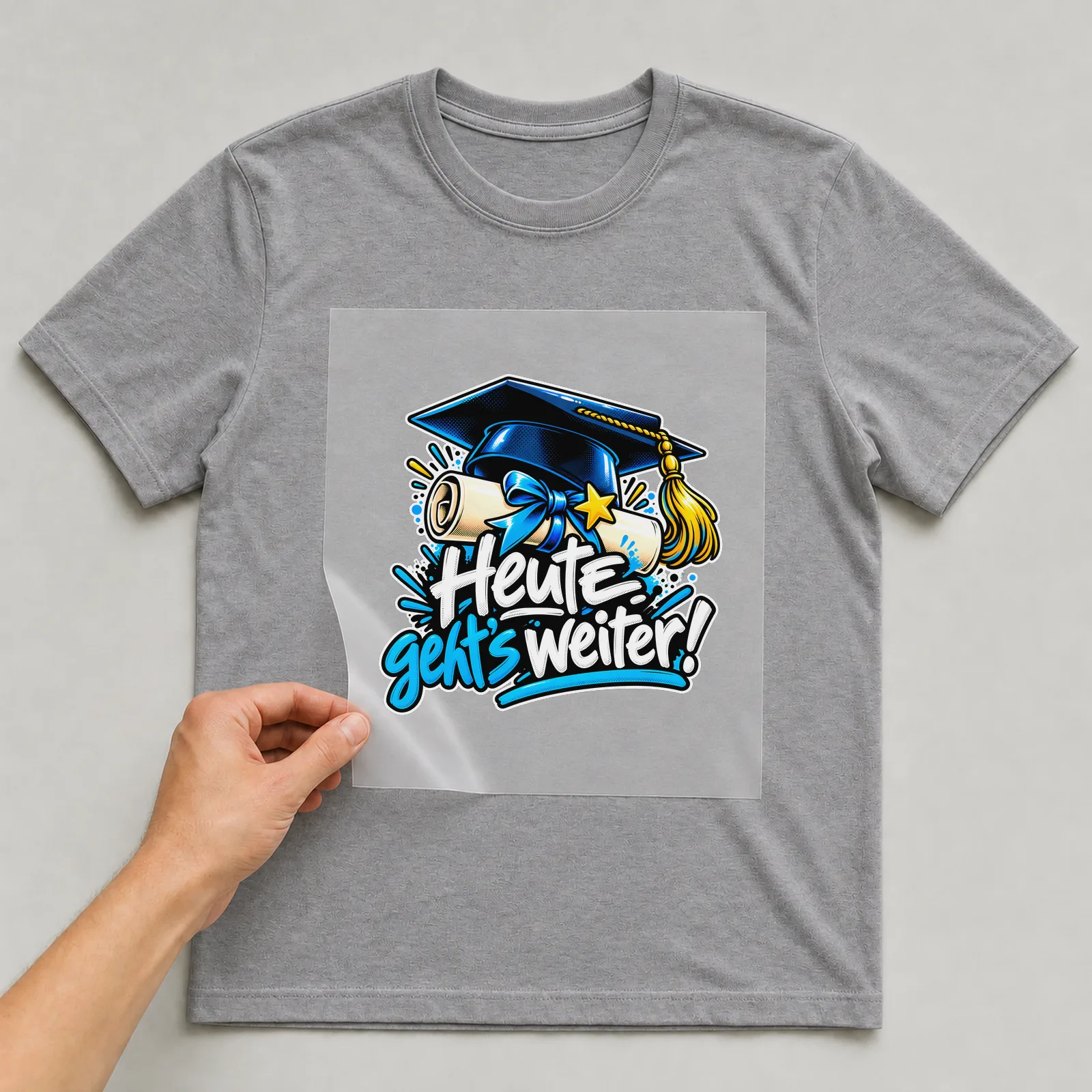 Bügelbild „Heute geht’s weiter!“ auf grauem T-Shirt, Folie wird aufgelegt