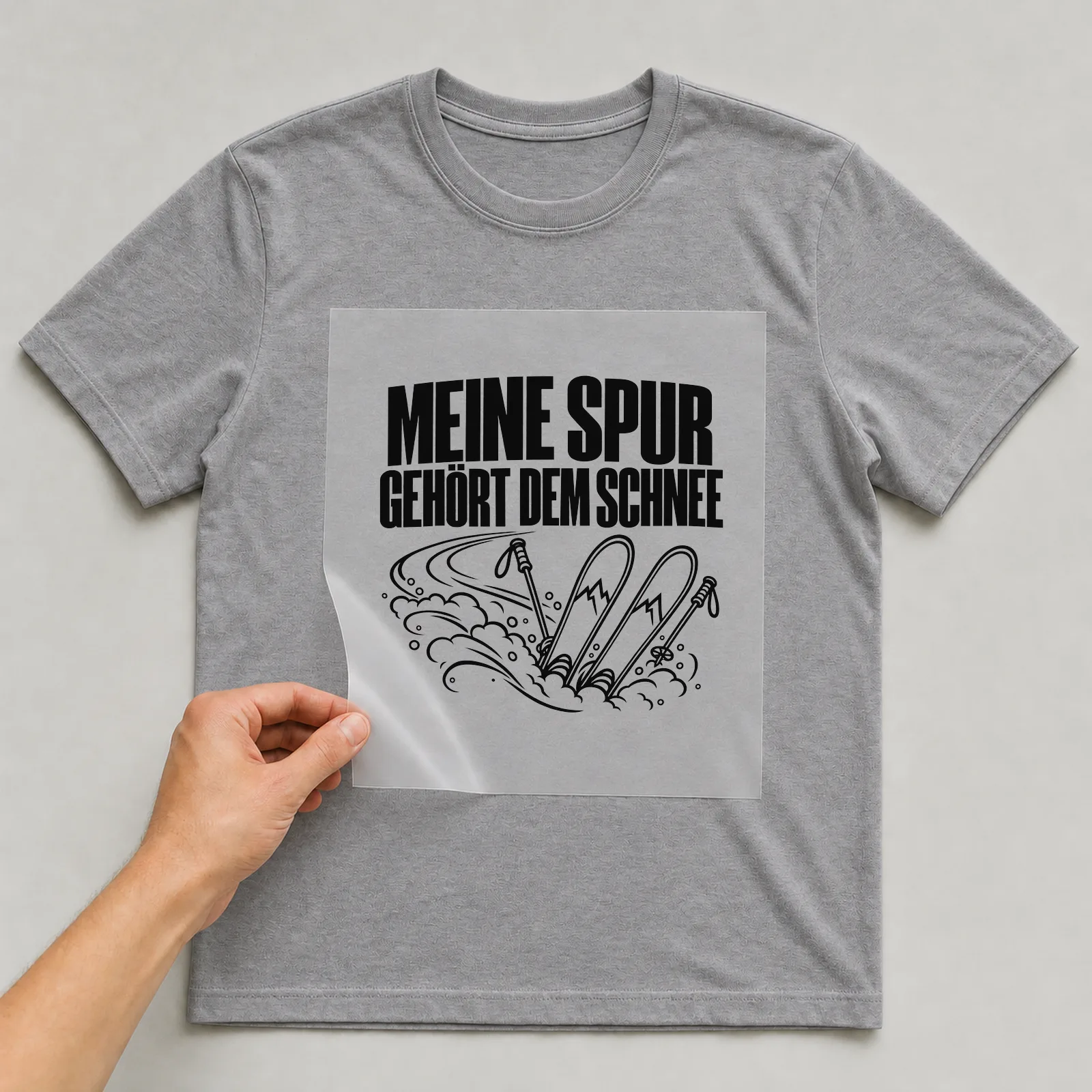 Bügelbild „Meine Spur gehört dem Schnee“ auf grauem T-Shirt, Folie wird aufgelegt